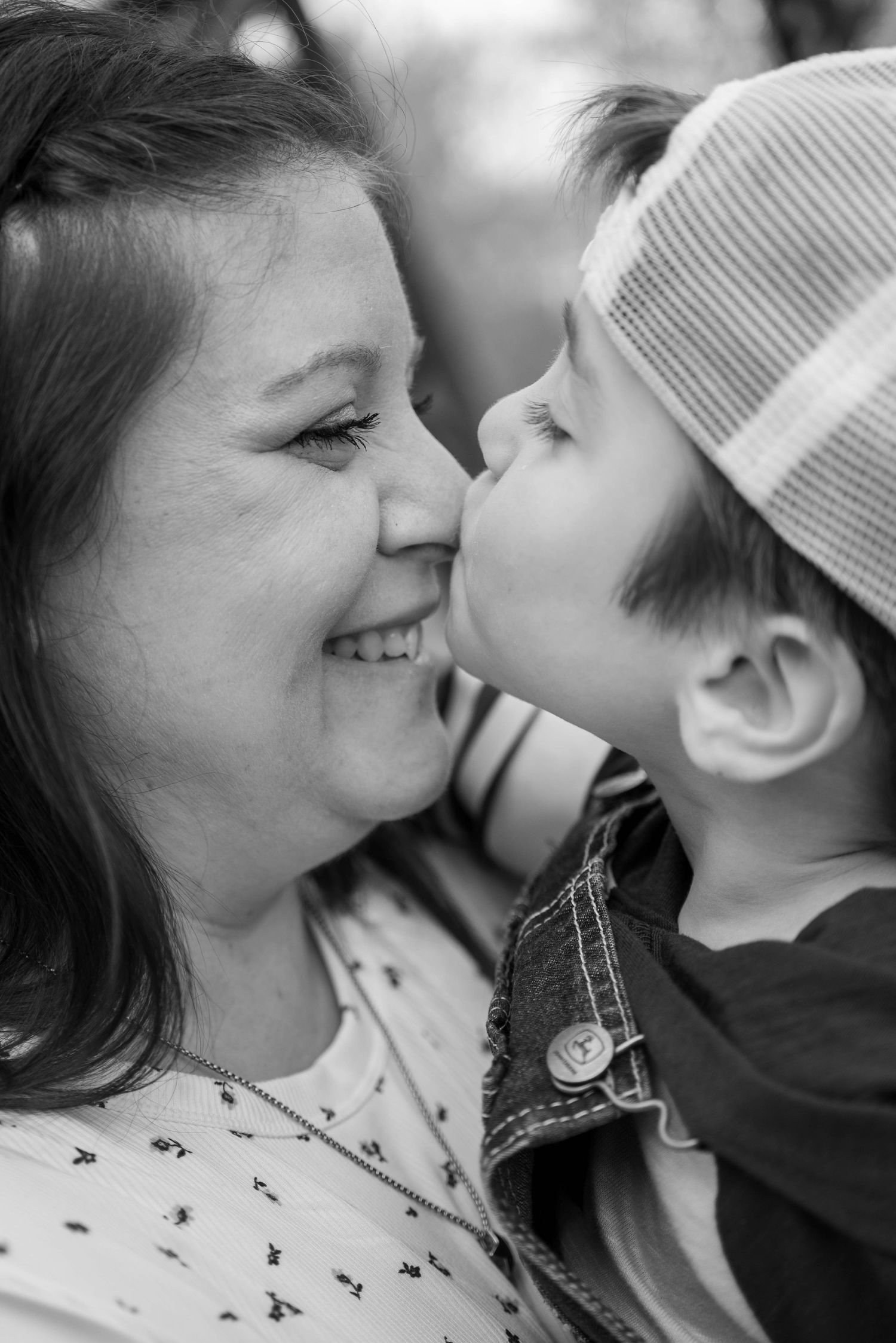 Black and white photo of a young boy in a cap giving his smiling mother a sweet kiss on the cheek.