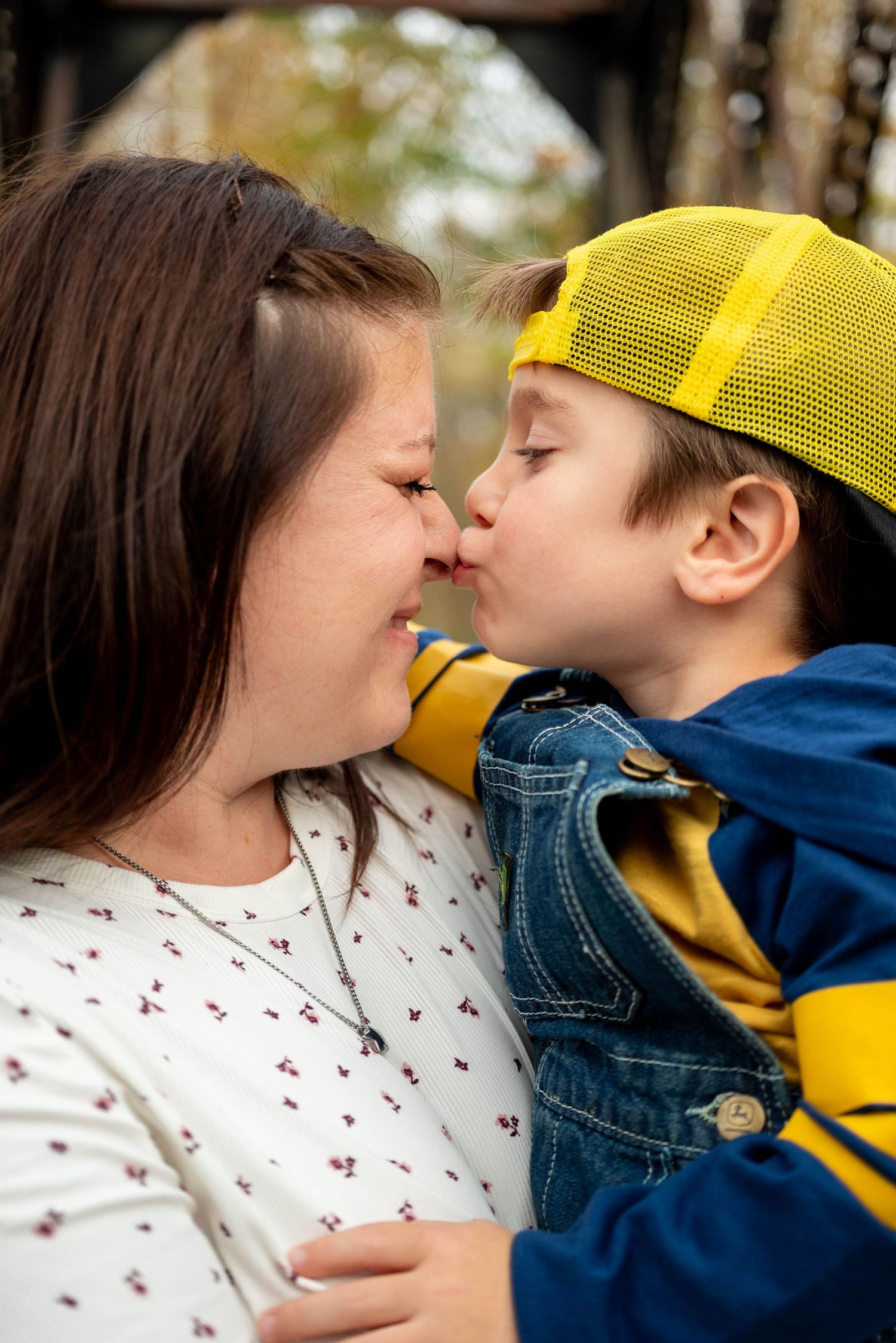 A young boy in a yellow cap gives his smiling mother a sweet nose kiss outdoors in autumn.