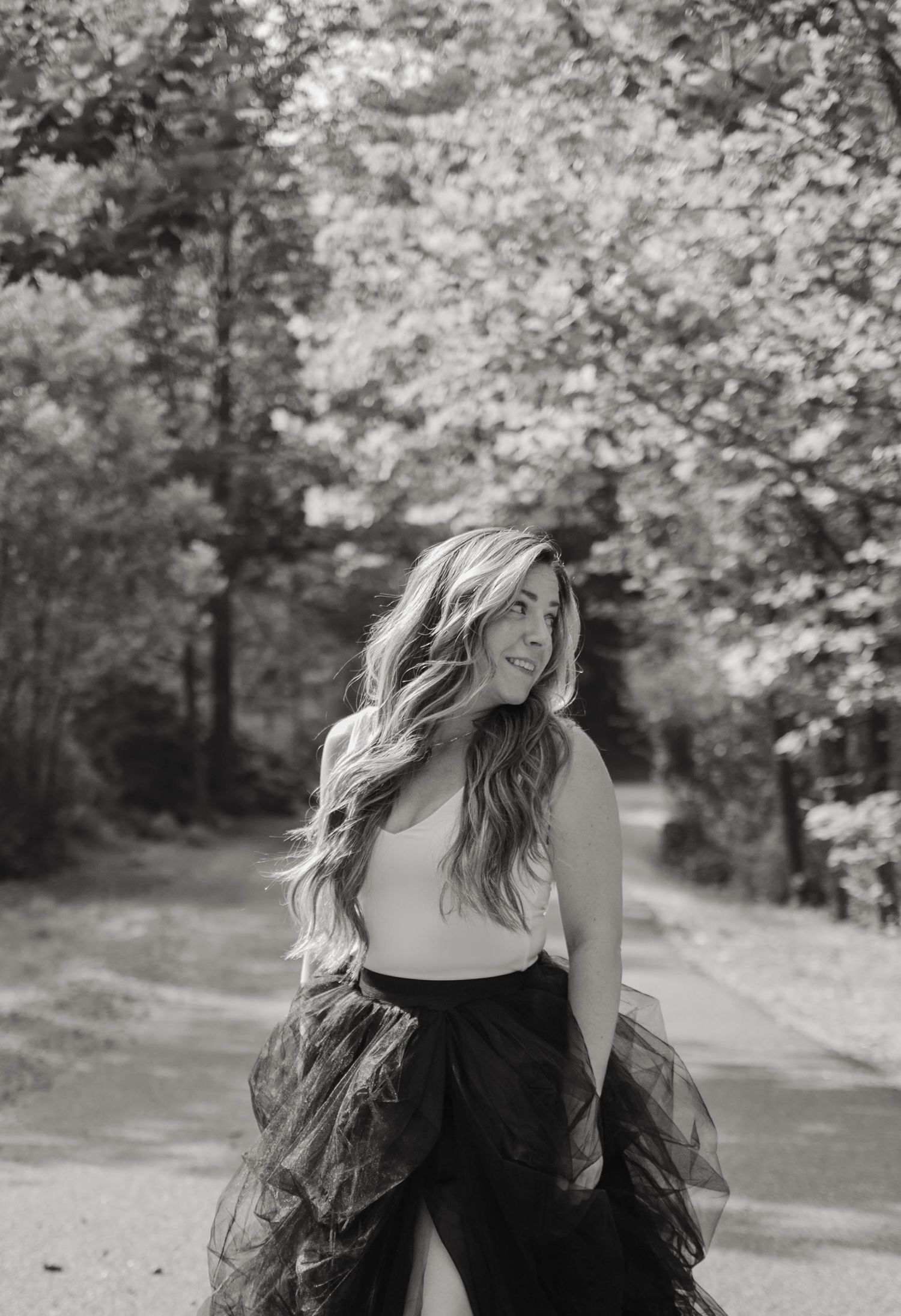 Black and white portrait of a woman with long wavy hair in a tulle skirt on a forest path.
