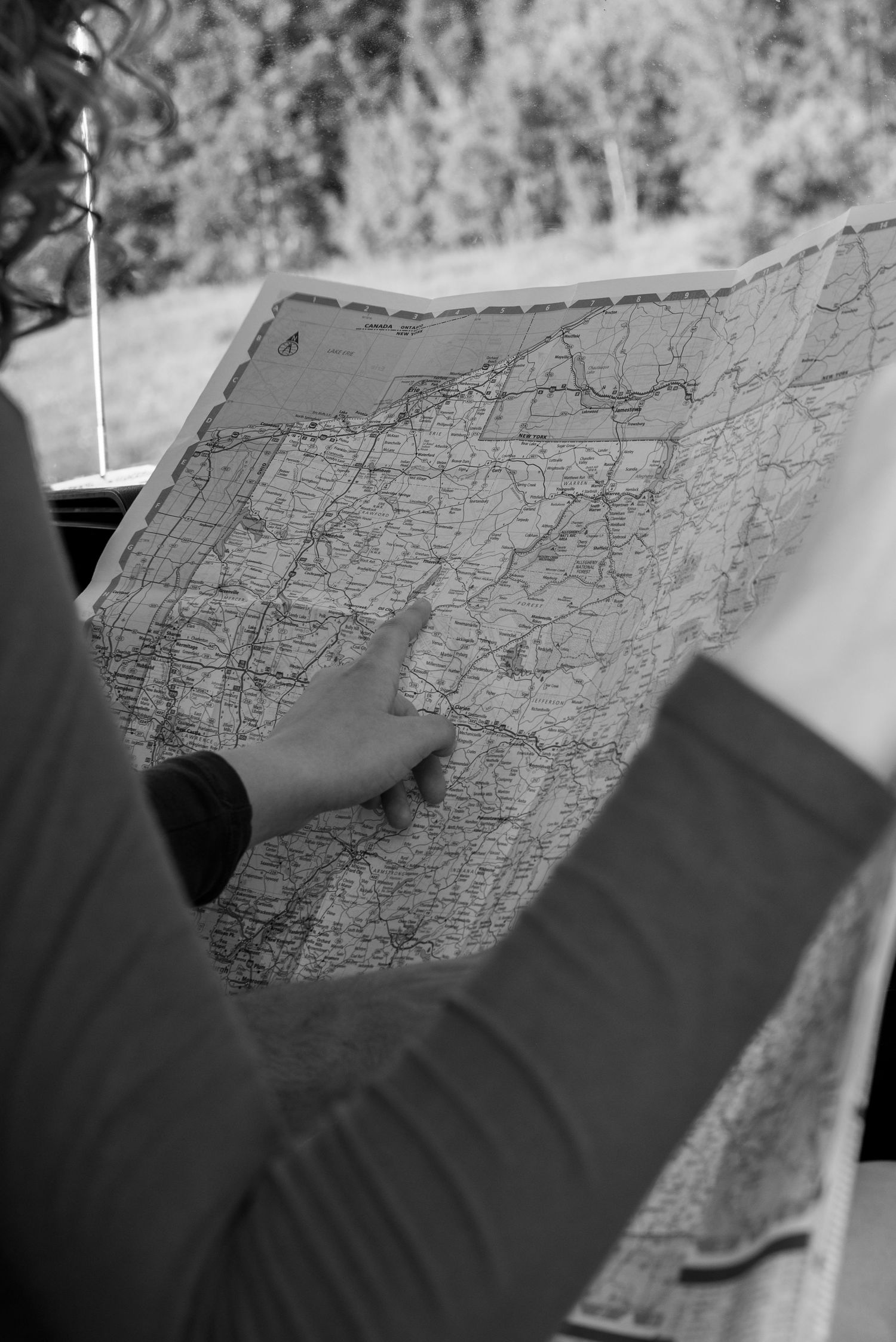 A person pointing at a location on a detailed road map in black and white photography.
