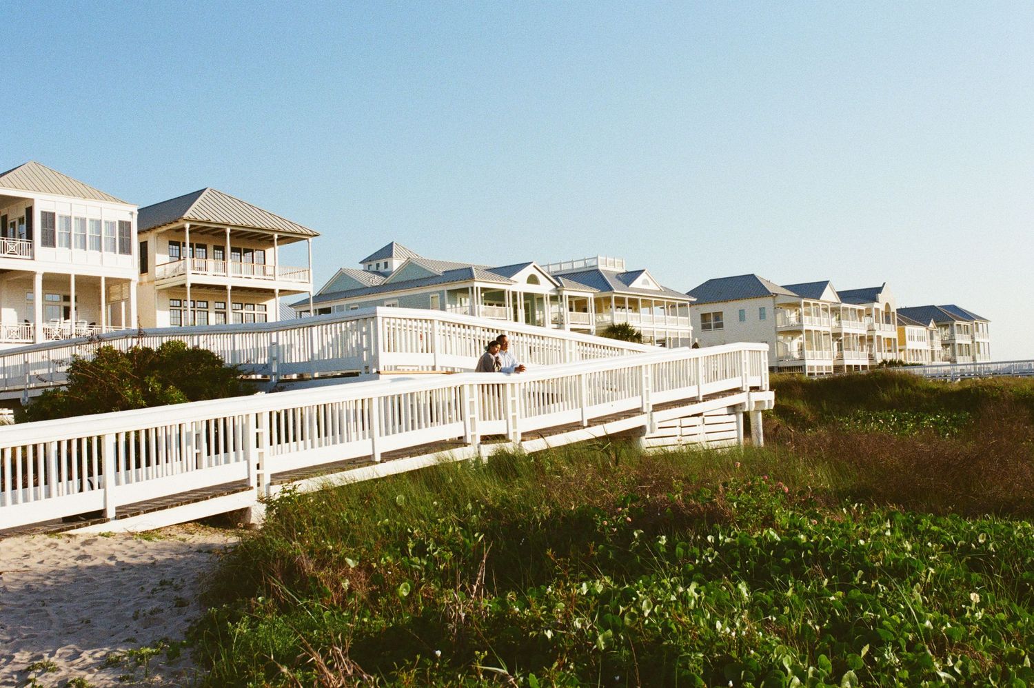a couple leaning over a white fence at beach captured on  film