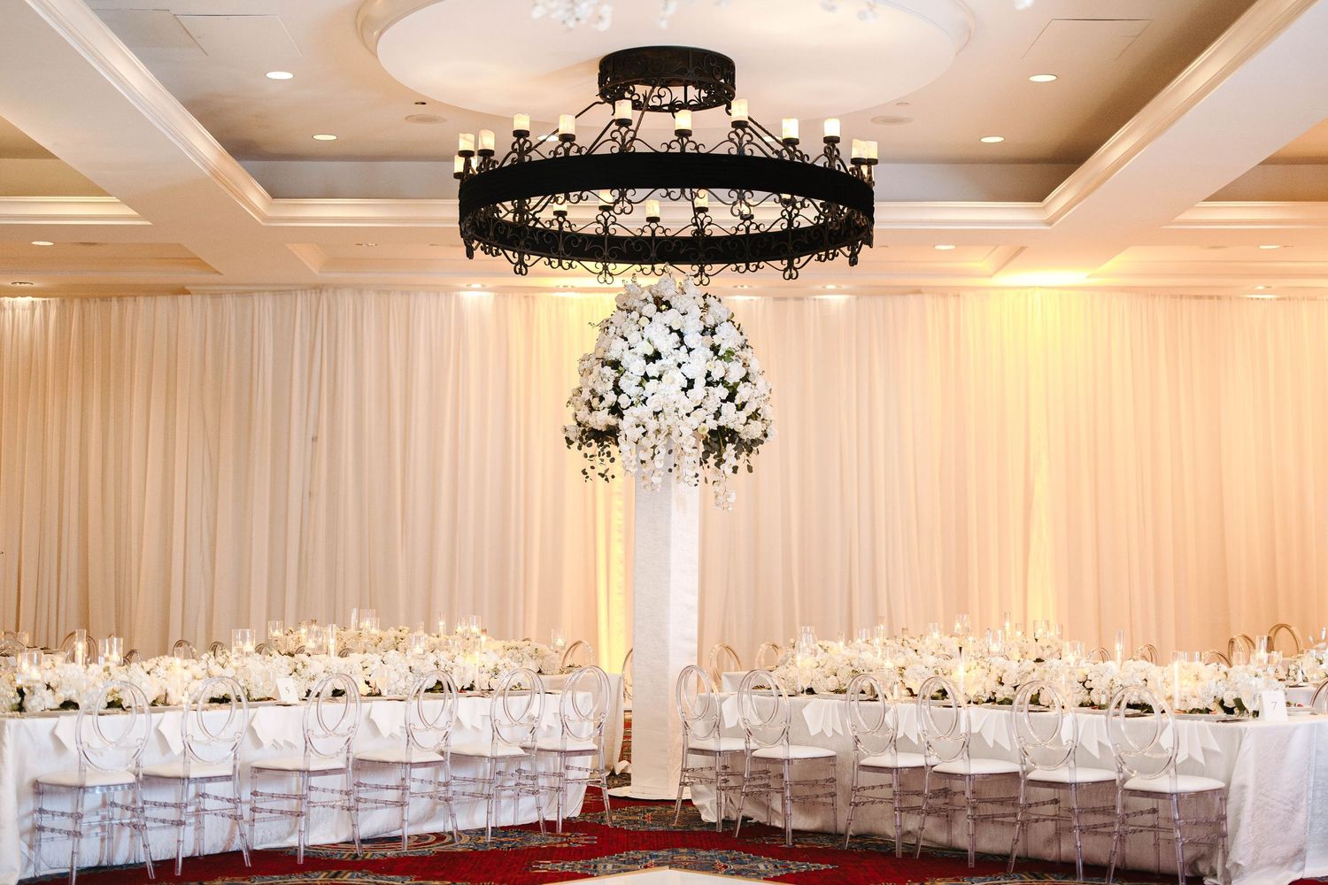 Elegant indoor wedding ceremony setup with white draping, chandelier, and floral ceremony arch in a formal ballroom venue.