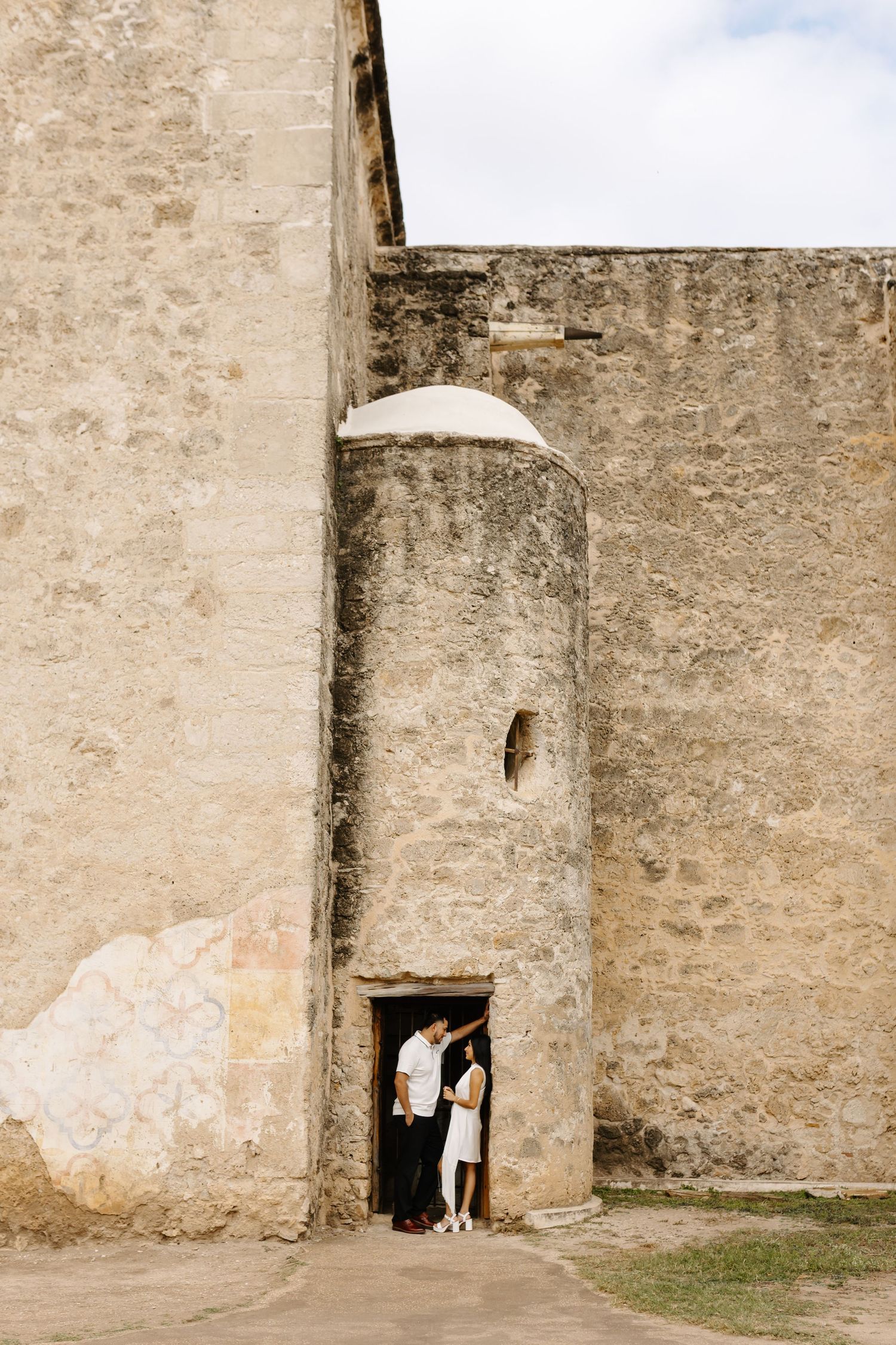 Couple standing in doorway of tall ancient stone tower, rustic fortress walls, dramatic vertical scene, romantic destination portrait.