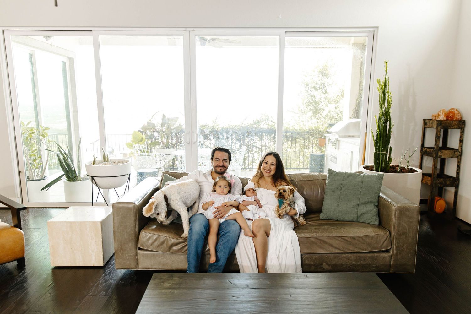 a portrait of a family in home, in their couch with babies and dog