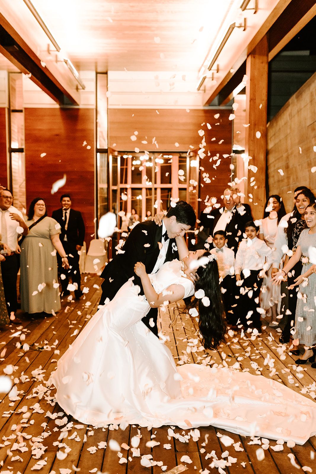 oyful wedding reception moment with bride and groom dancing under falling confetti surrounded by cheering guests in a warm lit ballroom.