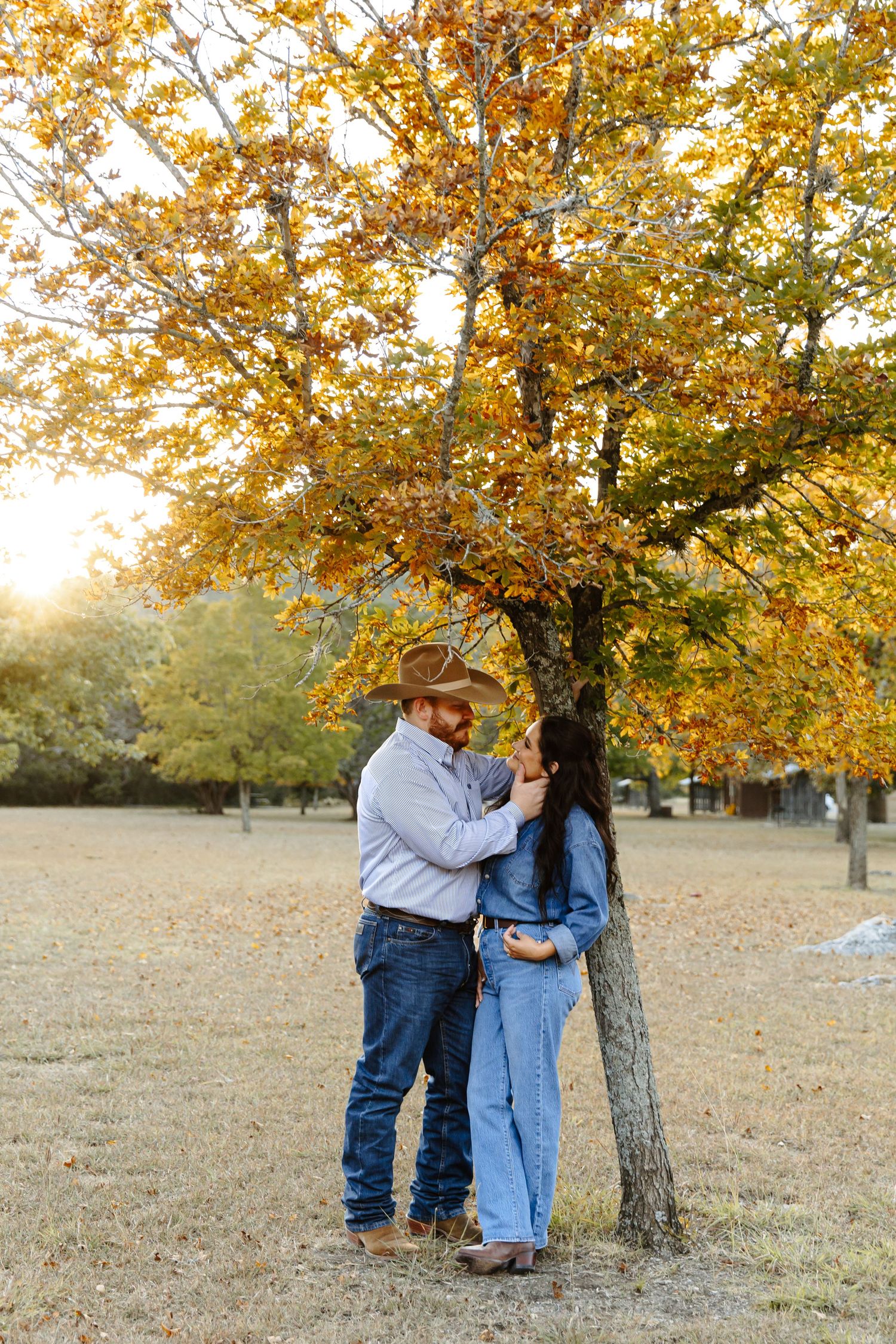 Couple standing under a foliage tree and dramatic vertical scene, both wearing jeans.