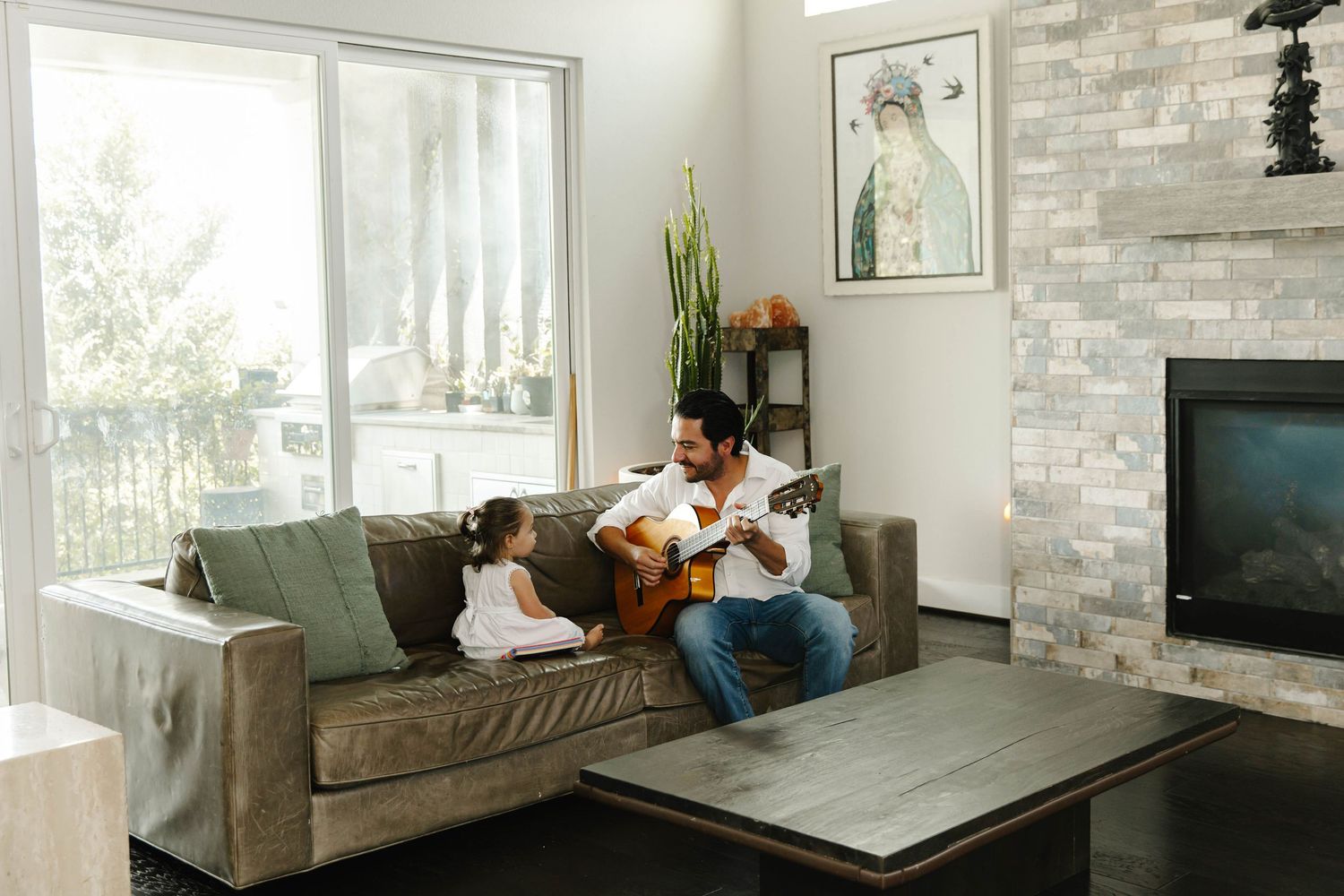 a candid photo of a father playing acoustic guitar while a toddler sits on his lap touching the strings, cozy family moment in