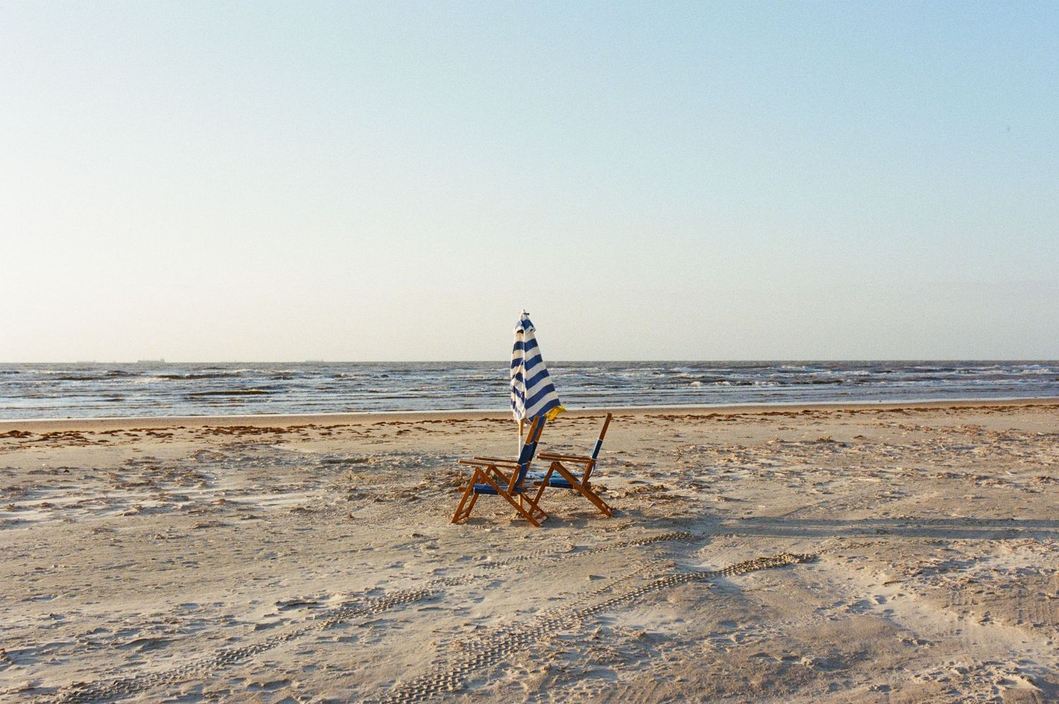 a landscape photograph of the Galveston beach ocean and in the middle is two wooden chairs