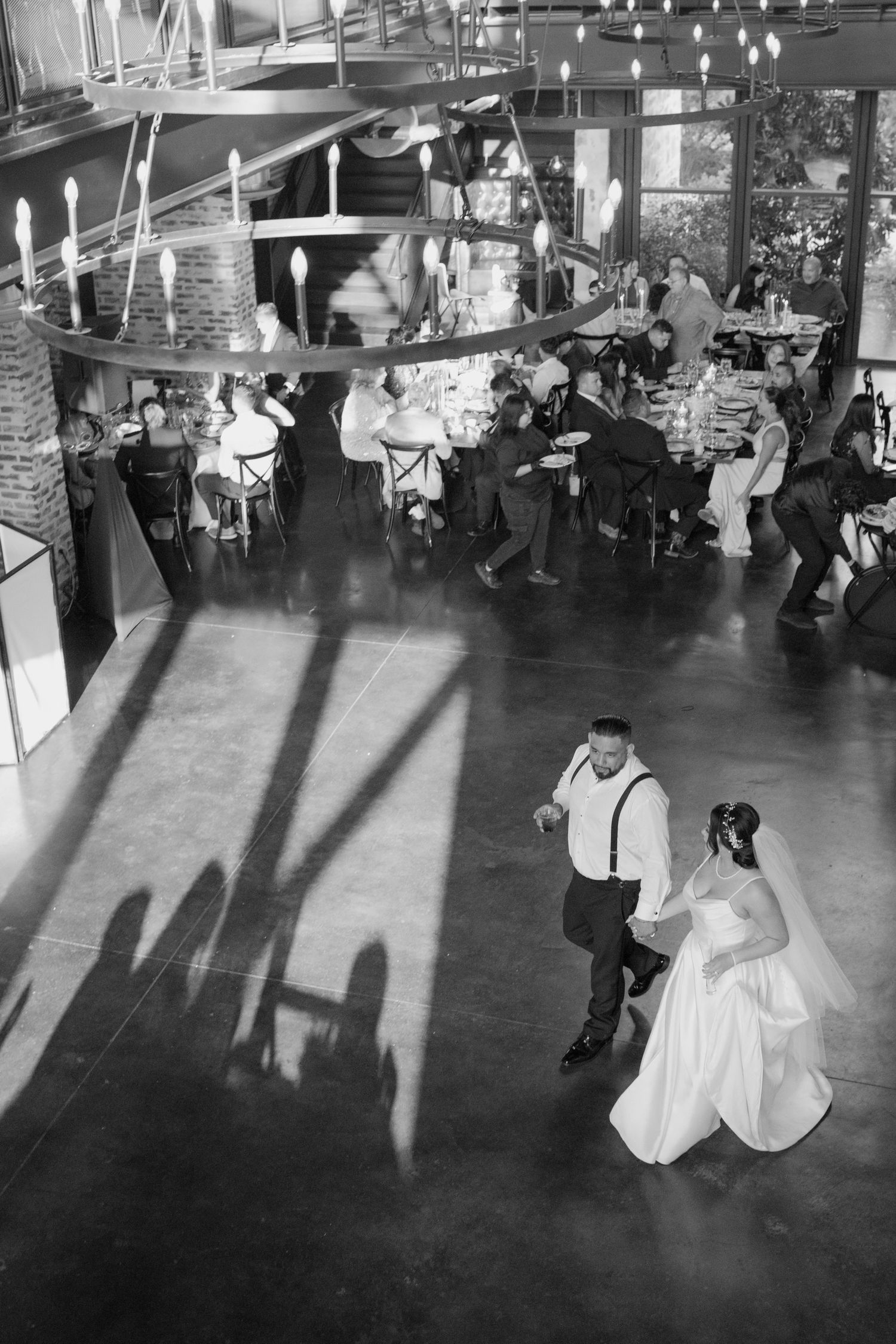 Black and white wedding reception first dance with bride and groom on a ballroom floor, long dramatic shadows from window light, guests seat