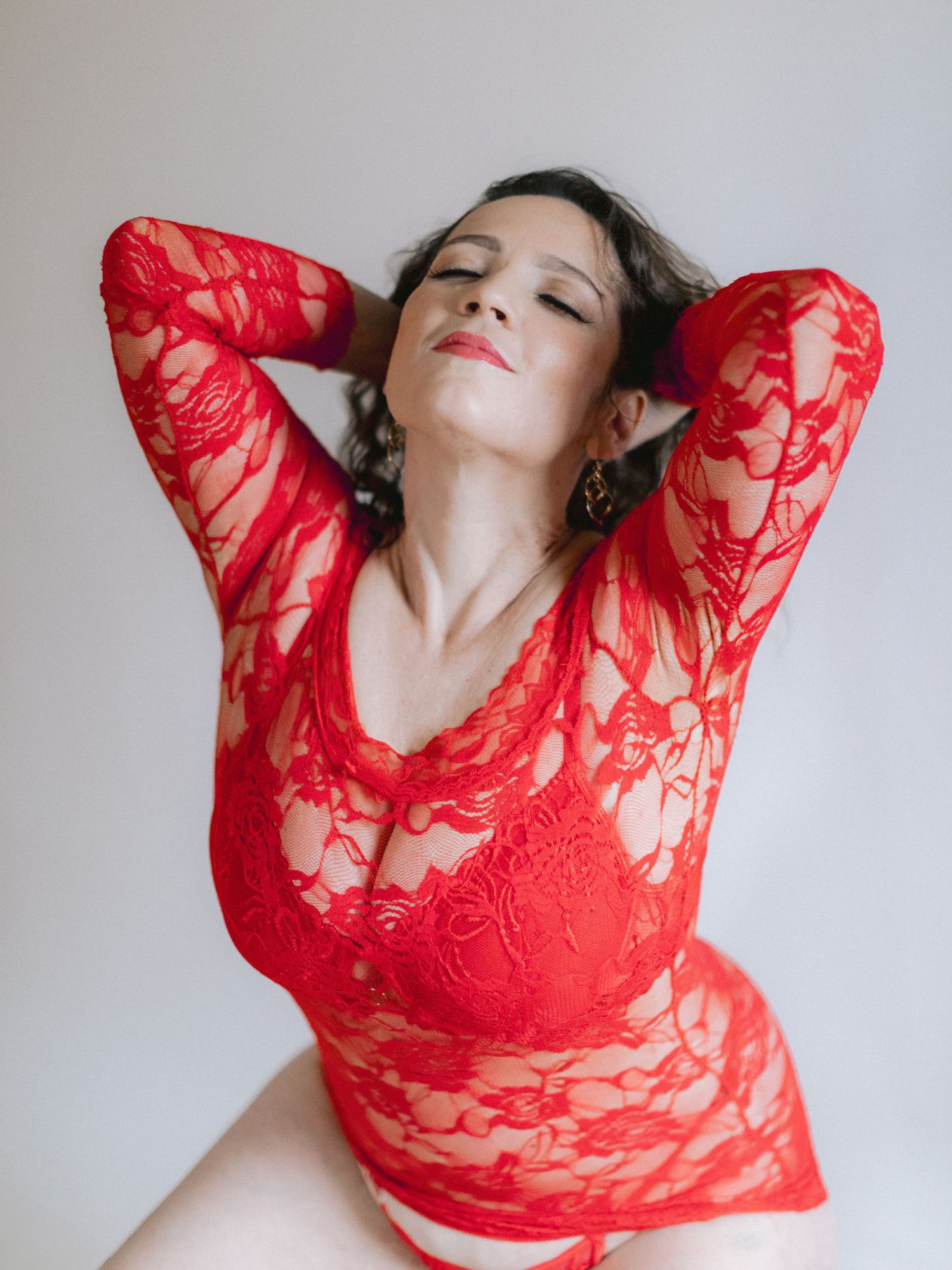 A boudoir portrait showing a woman in a red lace top against a light background.