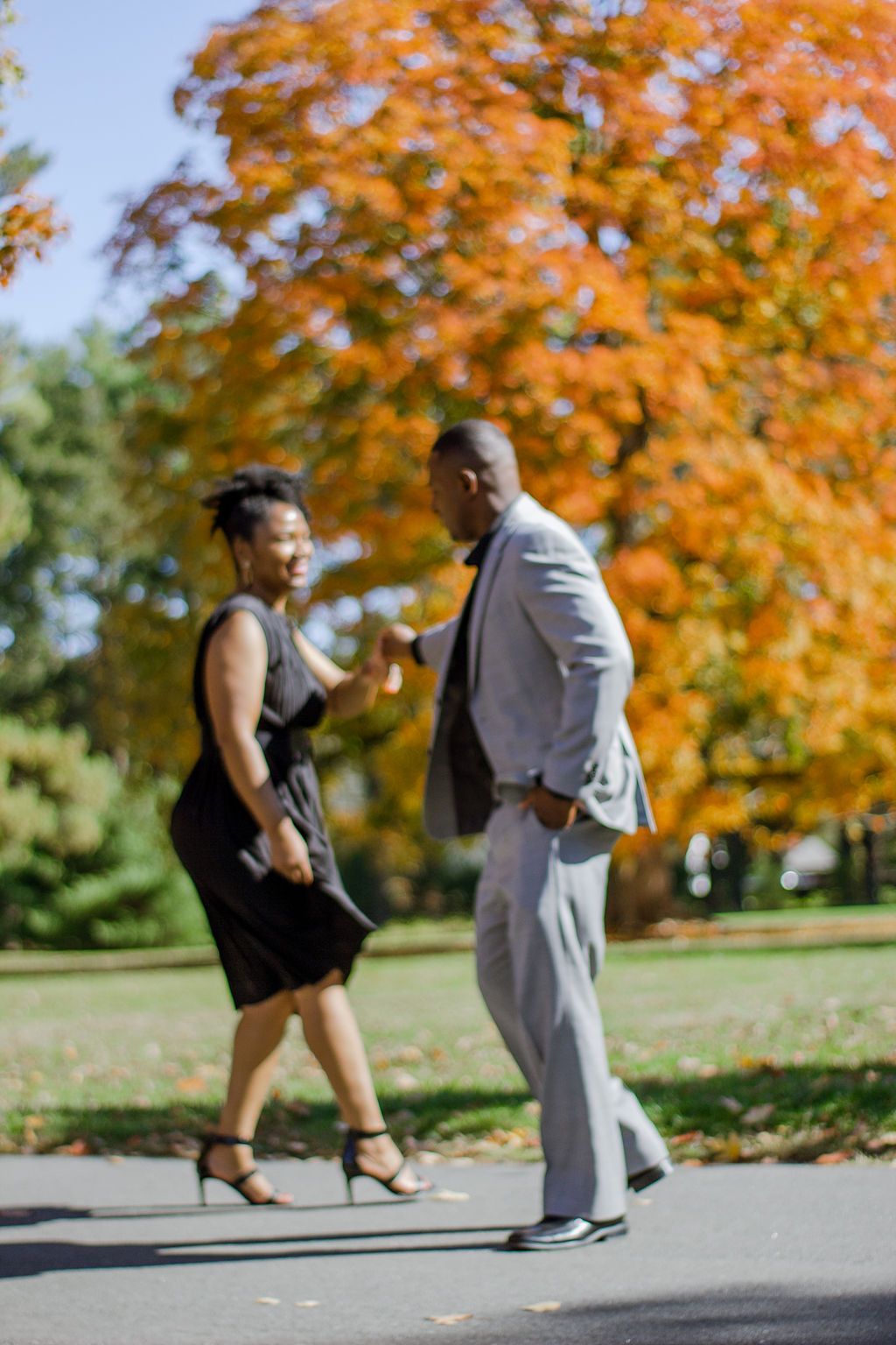Couple dancing together on a path with vibrant autumn foliage in the background.