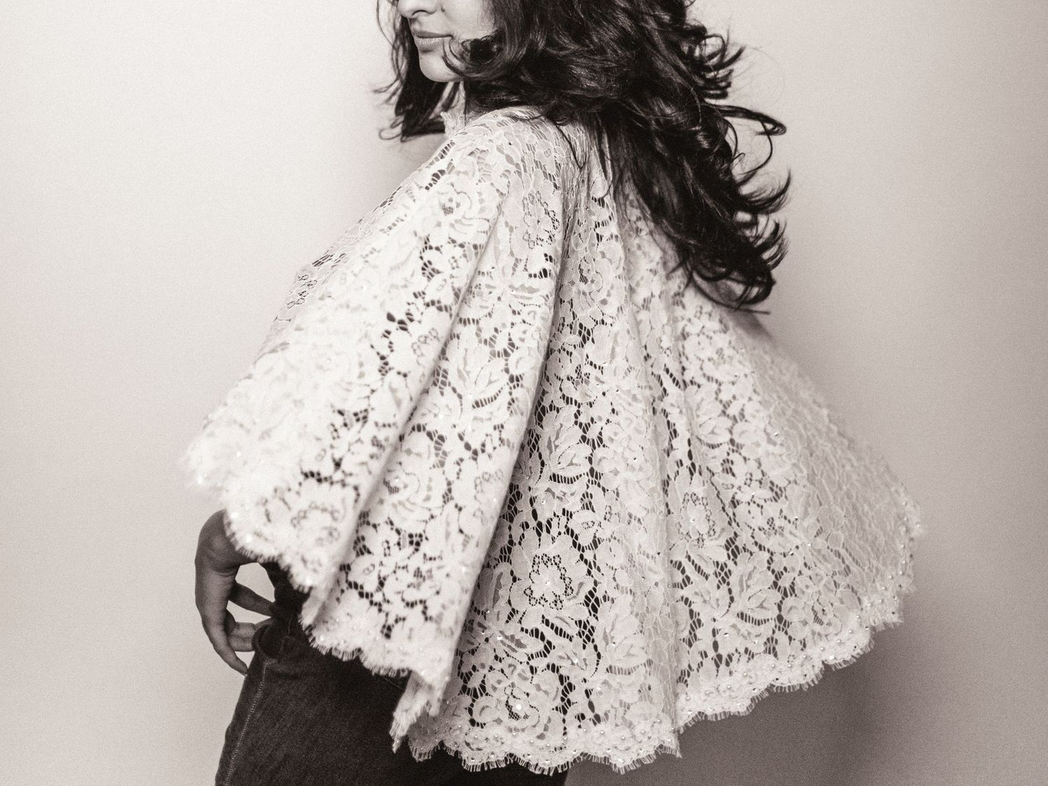 Pregnant woman in white lace bell-sleeve top shows baby bump in elegant black and white side profile portrait.