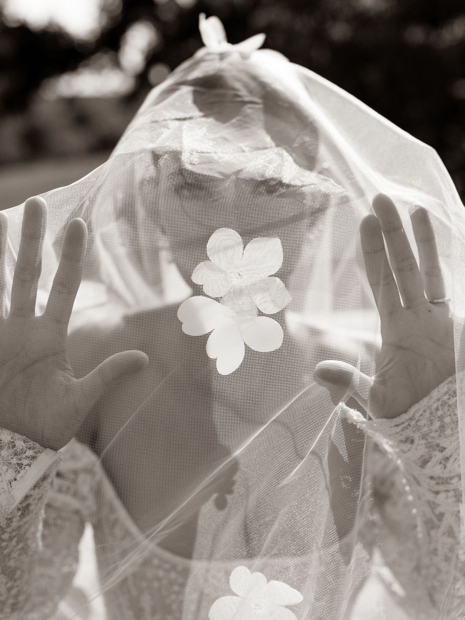 A black and white artistic wedding photo showing delicate white veils and floral details in soft focus.