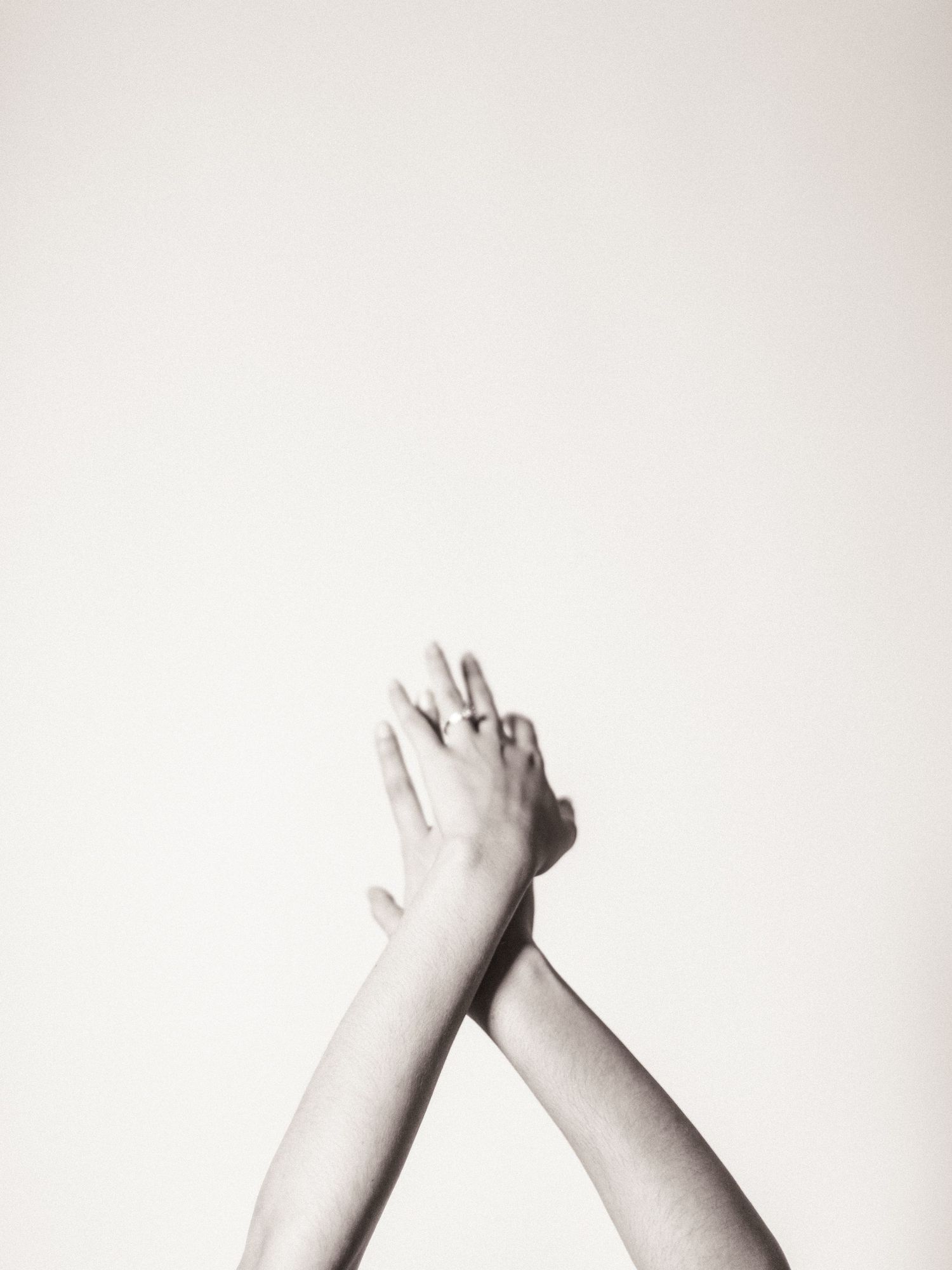 Black and white photo of two hands raised and intertwined against a light background.