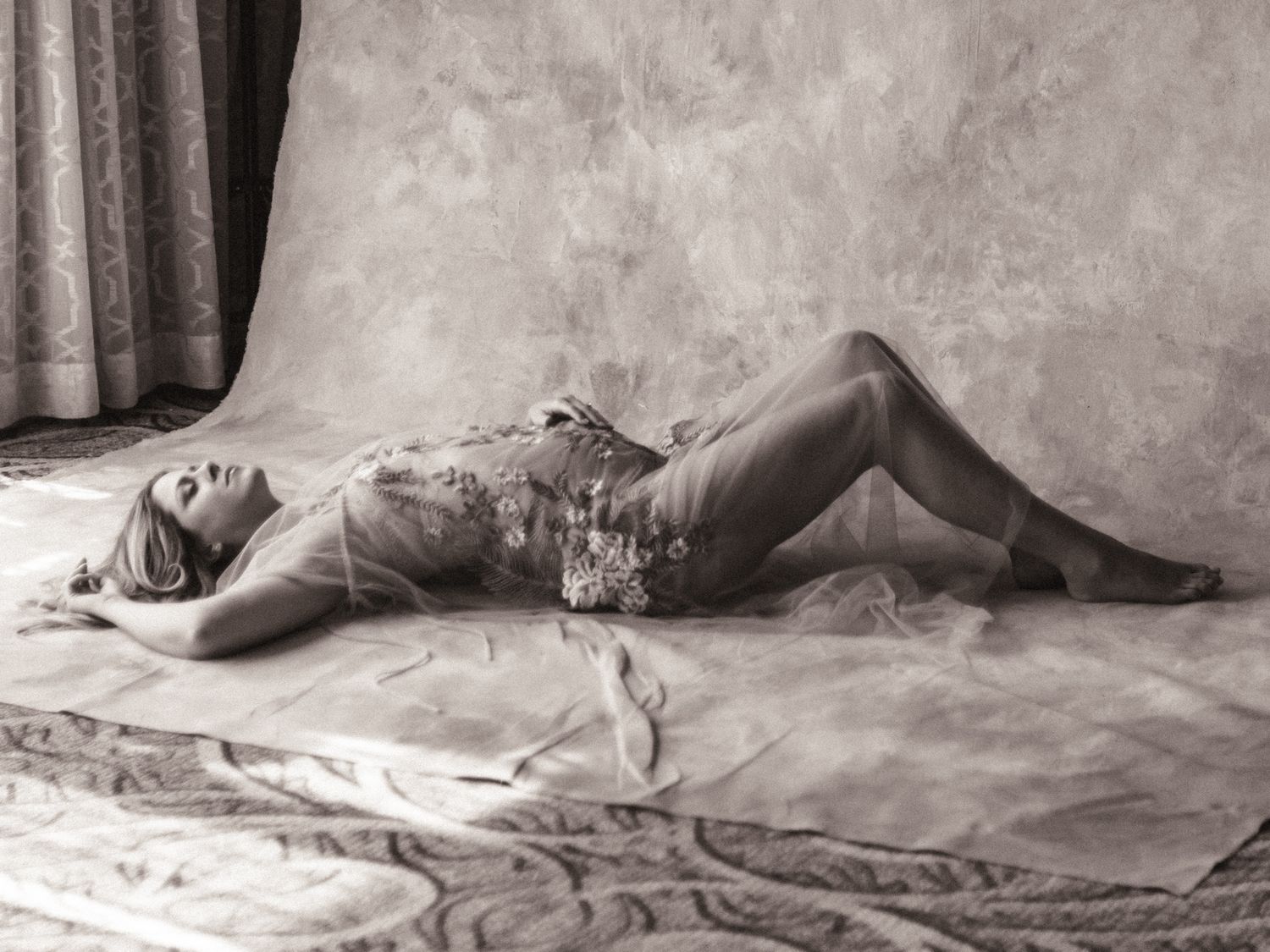 Black and white boudoir photo of a woman reclining gracefully on draped fabric in a studio setting.
