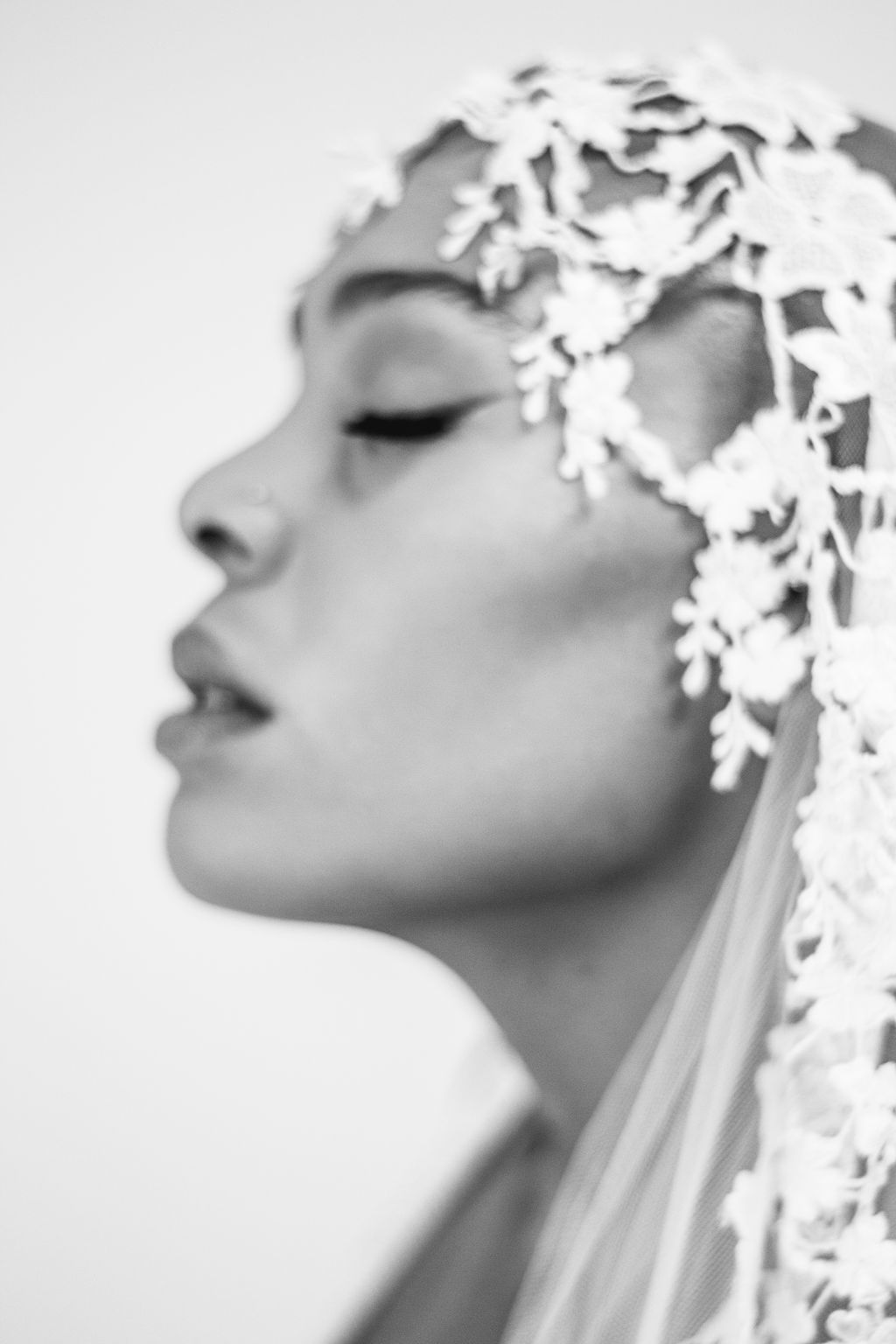 Black and white profile portrait of a woman wearing an ornate floral lace bridal veil.