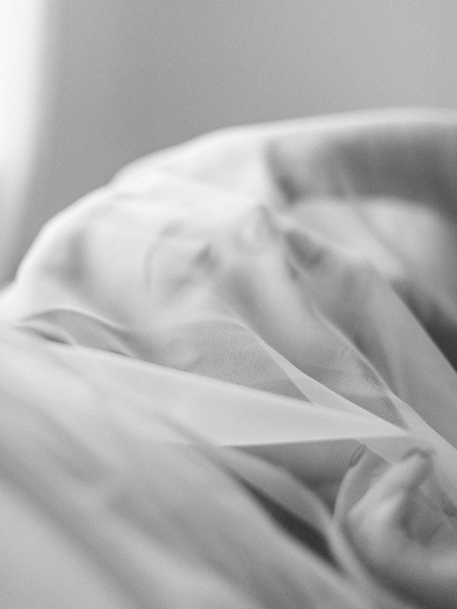 Close-up black and white photo of soft, flowing sheer white fabric with delicate folds and ethereal texture.