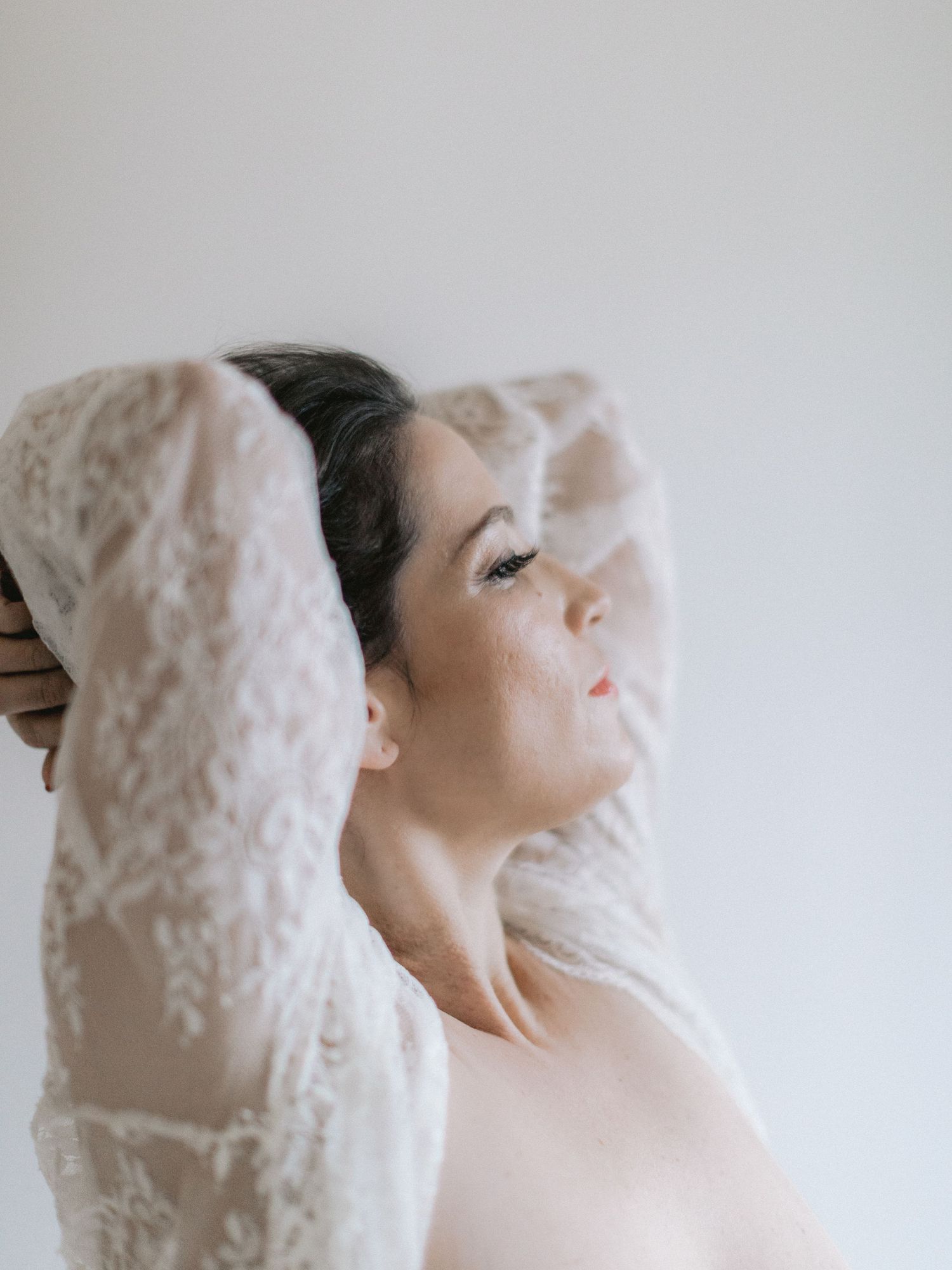 Intimate portrait showing ethereal profile view against white lace backdrop in soft lighting.