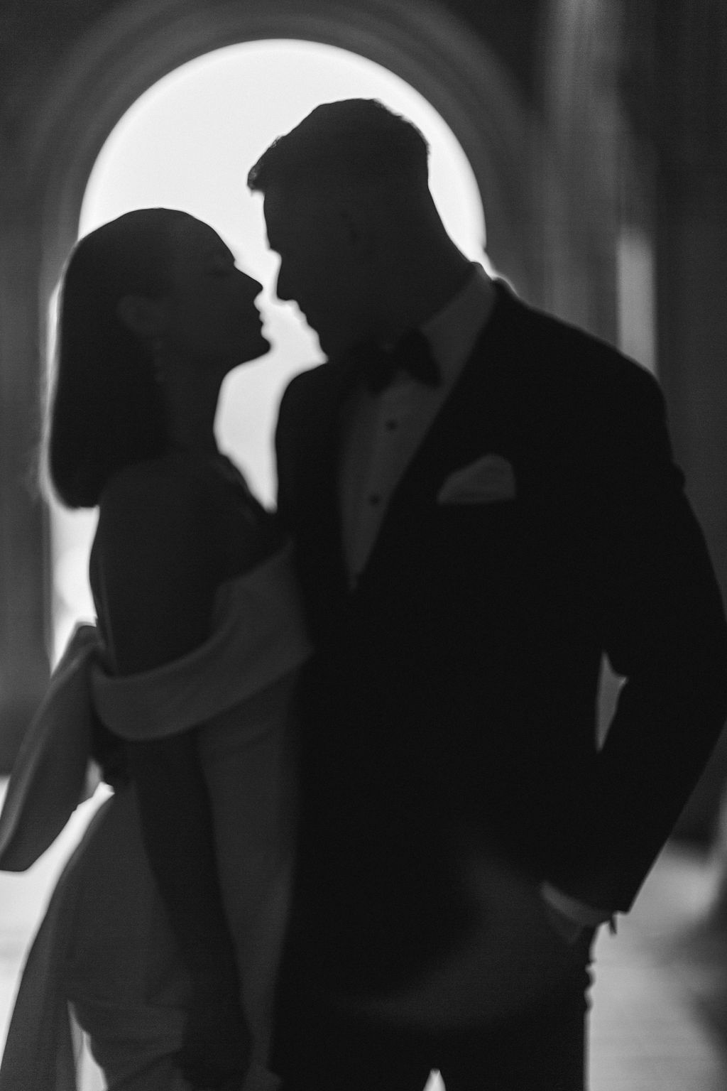 Dramatic black and white silhouette of elegant couple in formal wear sharing intimate moment in archway.