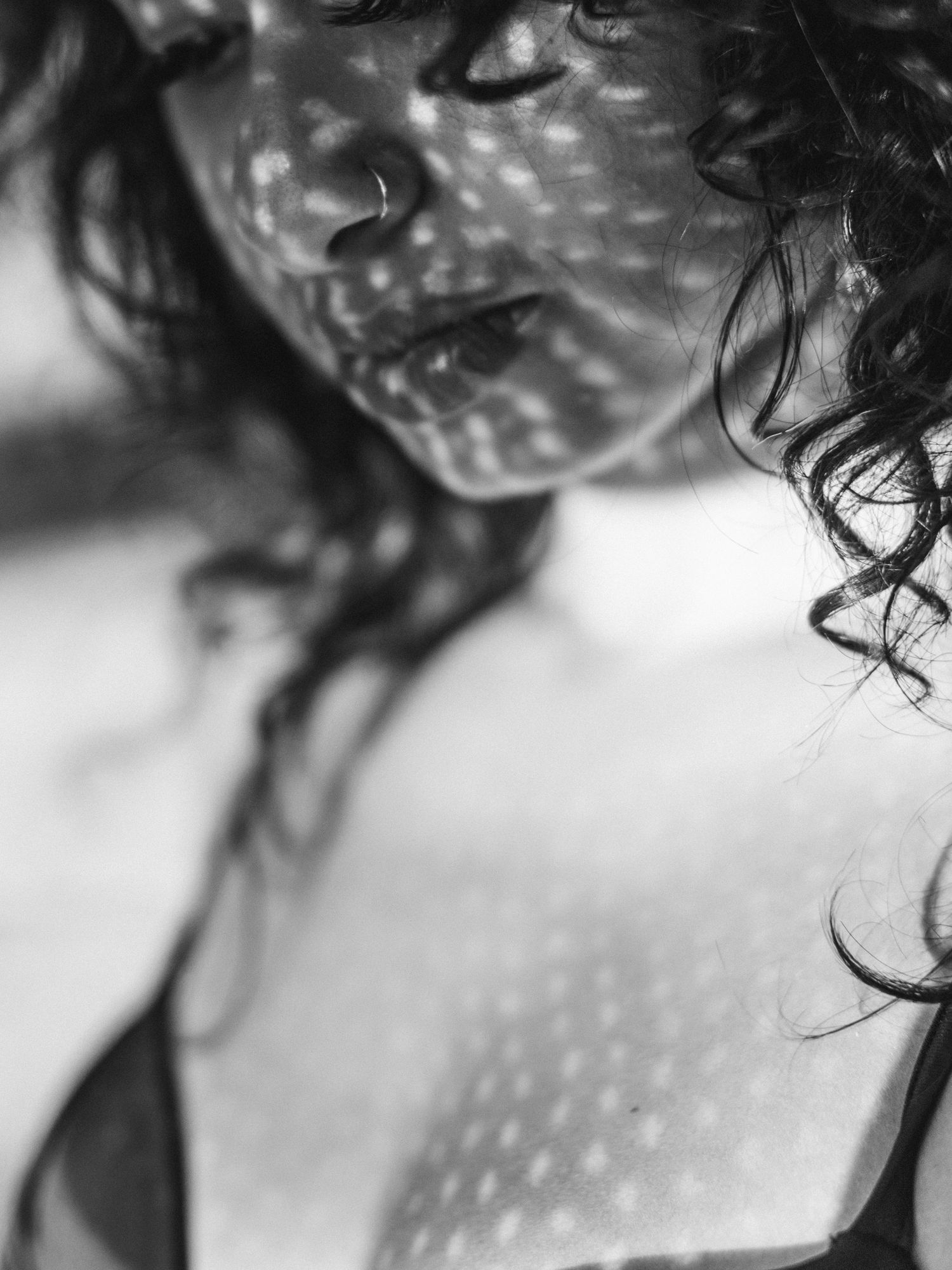 Black and white portrait of woman with curly hair and dappled light shadows on face.