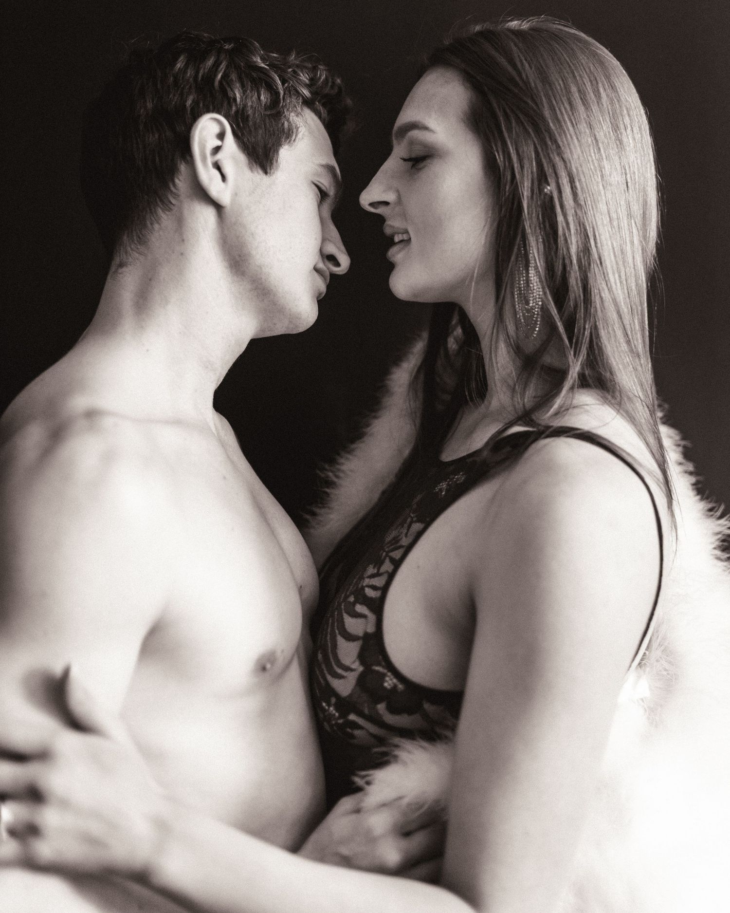 Black and white intimate portrait of shirtless man and woman in lace top almost kissing.