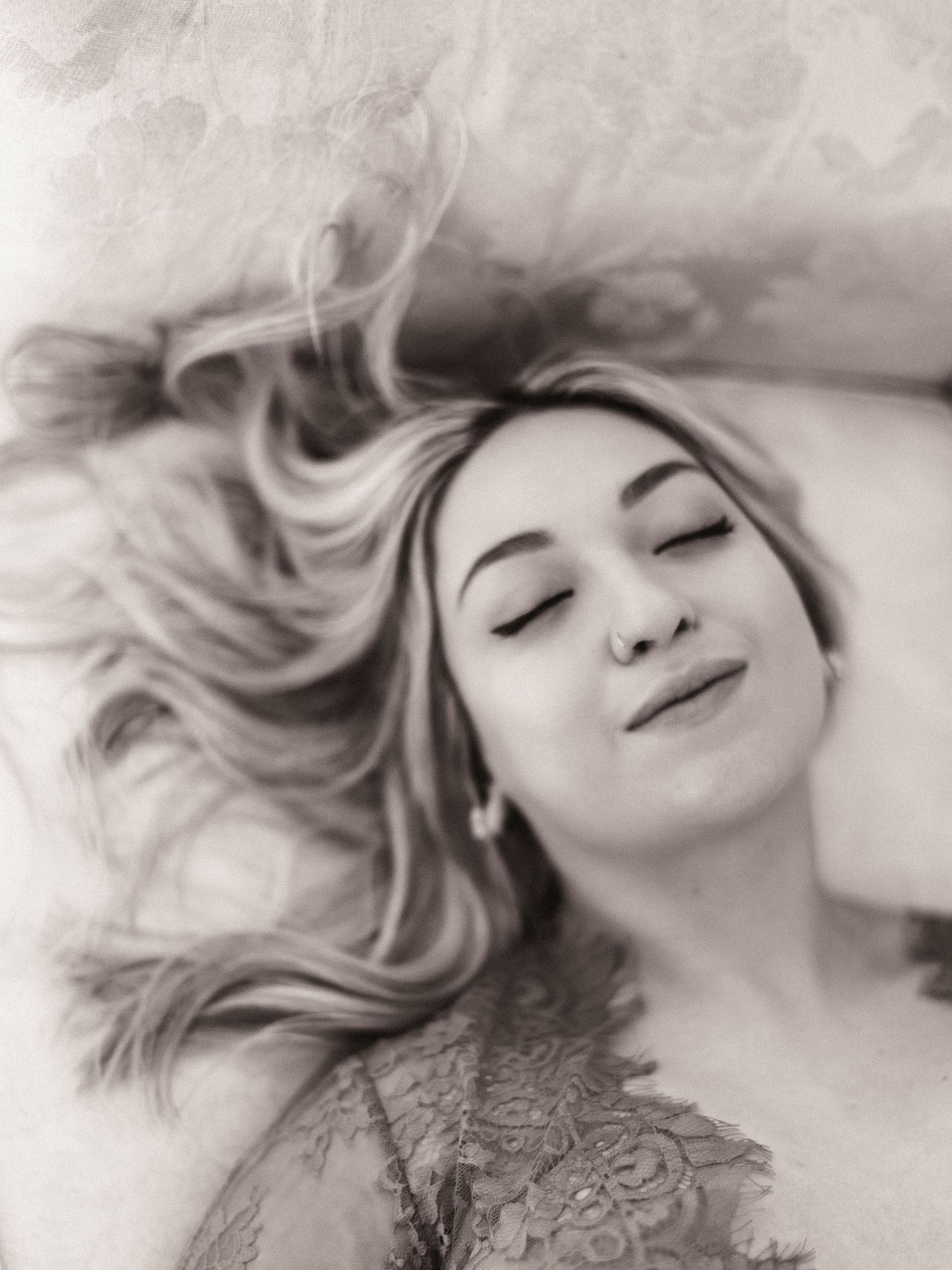 Blonde woman lying back with eyes closed in dreamy black and white boudoir portrait.