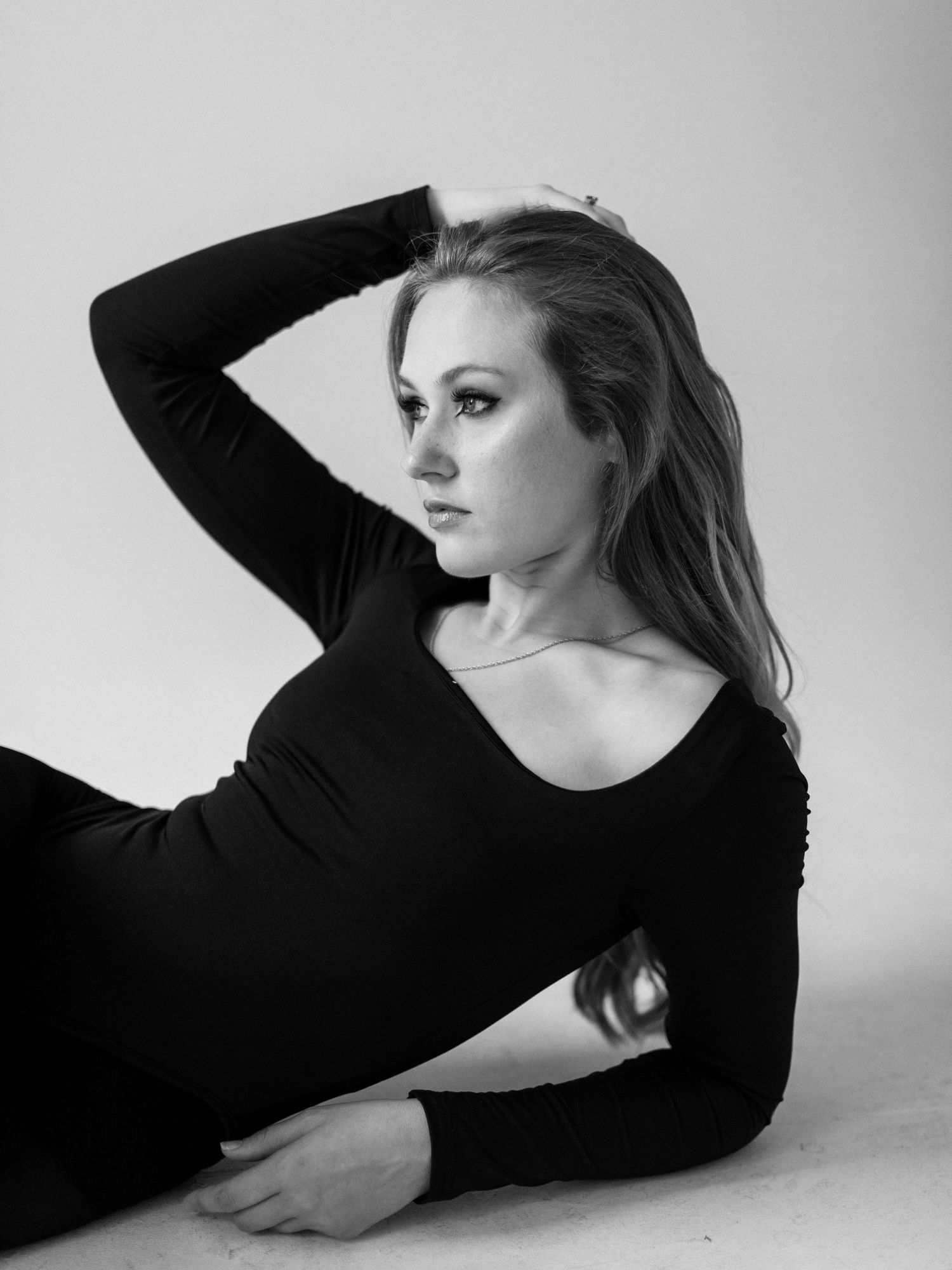 Black and white artistic portrait photo showing a figure in dark clothing reclining against a light background.