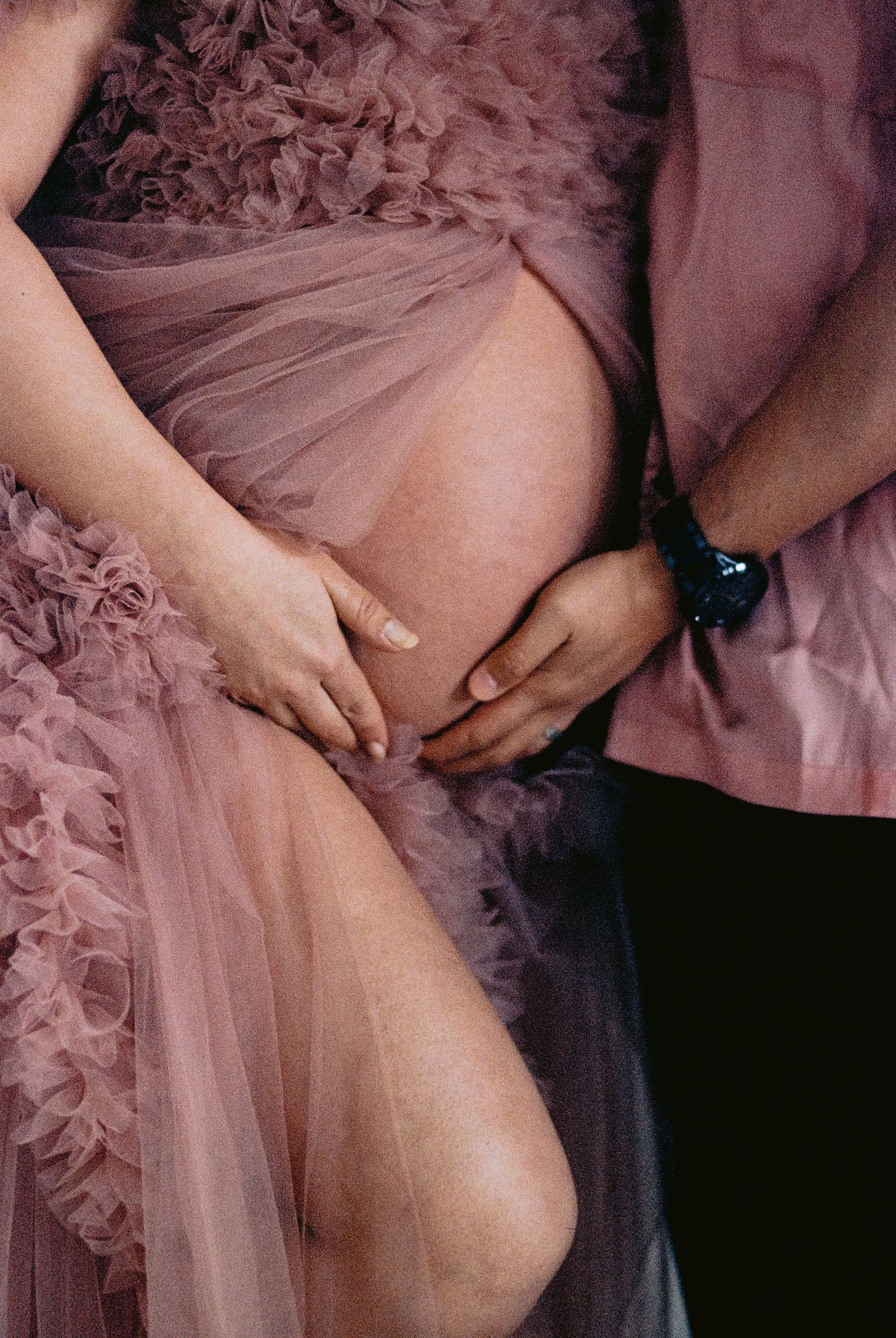 Couple tenderly cradling pregnant belly in matching pink outfits with ruffled maternity gown.