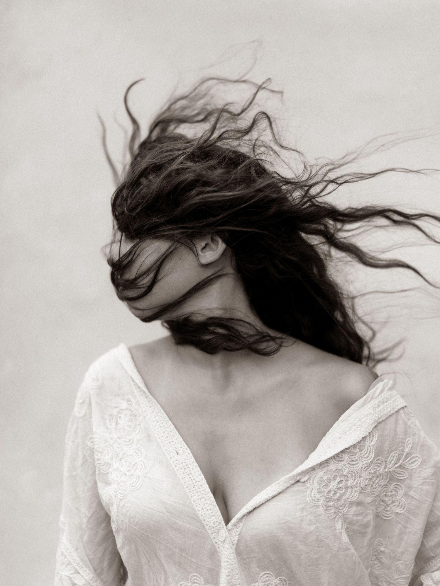 Black and white portrait of a woman Black and white photo of a woman in white dress with long dark hair blowing across her face in the wind.
