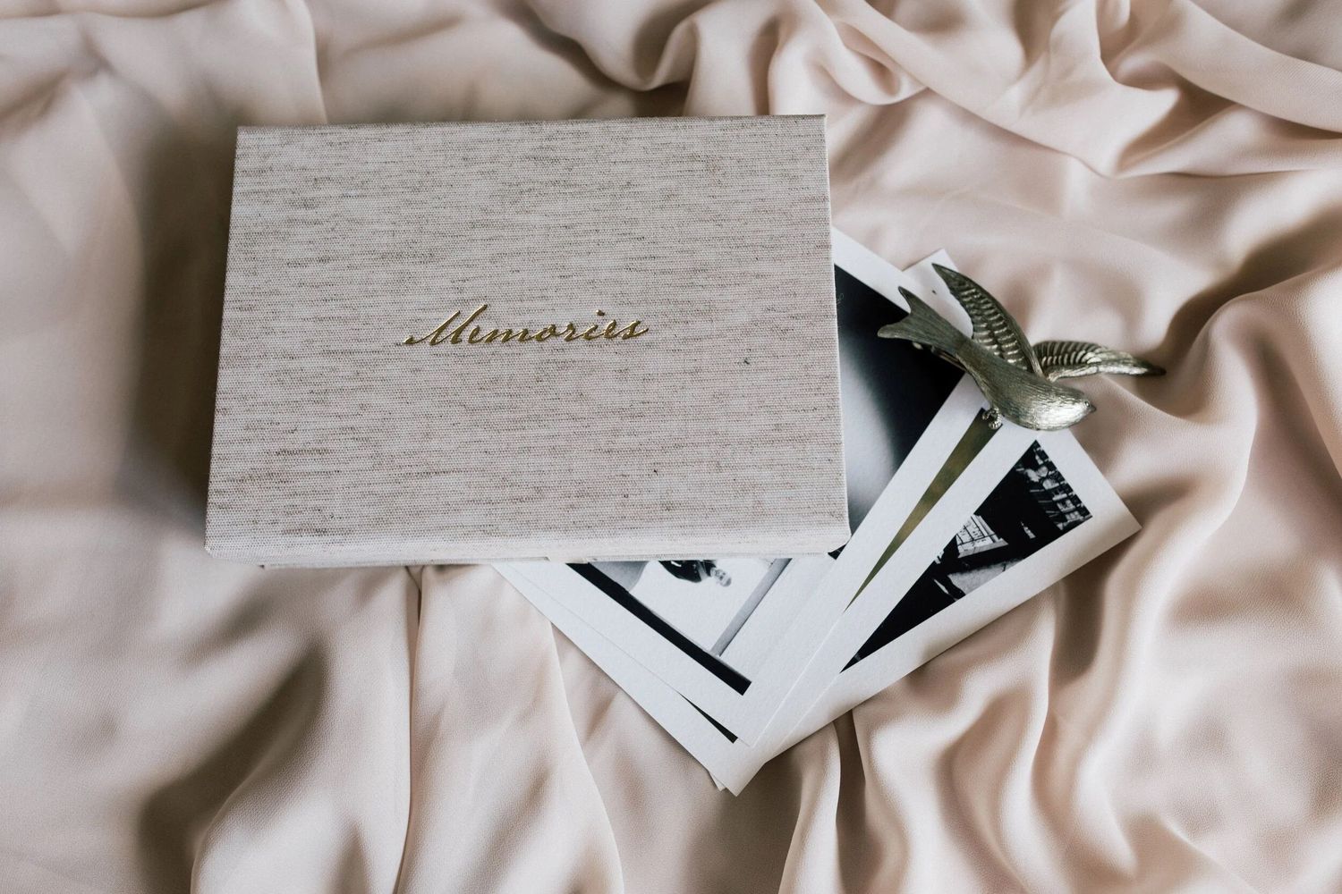 A linen-covered memory box with gold script reading Memories, resting on photos and pink silk fabric.