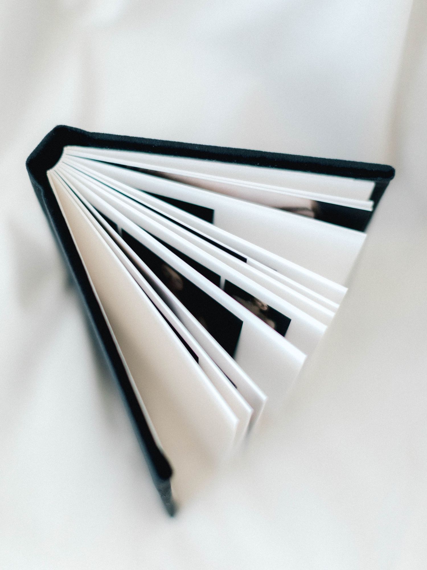 A small hardcover book with black binding lies open, its white pages fanned out in a triangular shape on a white surface.