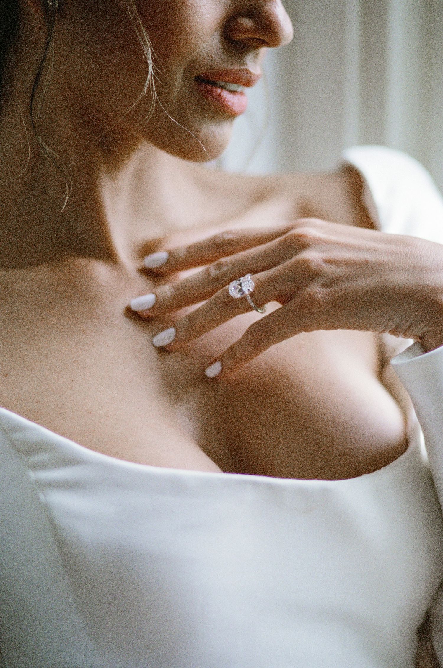 Bride in white strapless gown showcasing elegant diamond engagement ring against décolletage.