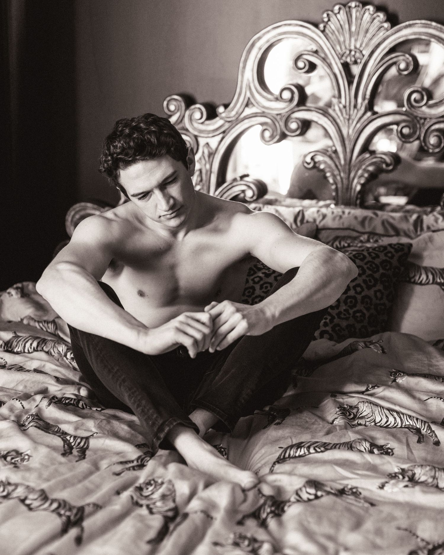 Black and white artistic photographs of a figure reclining against an ornate headboard on a bed with textured linens.