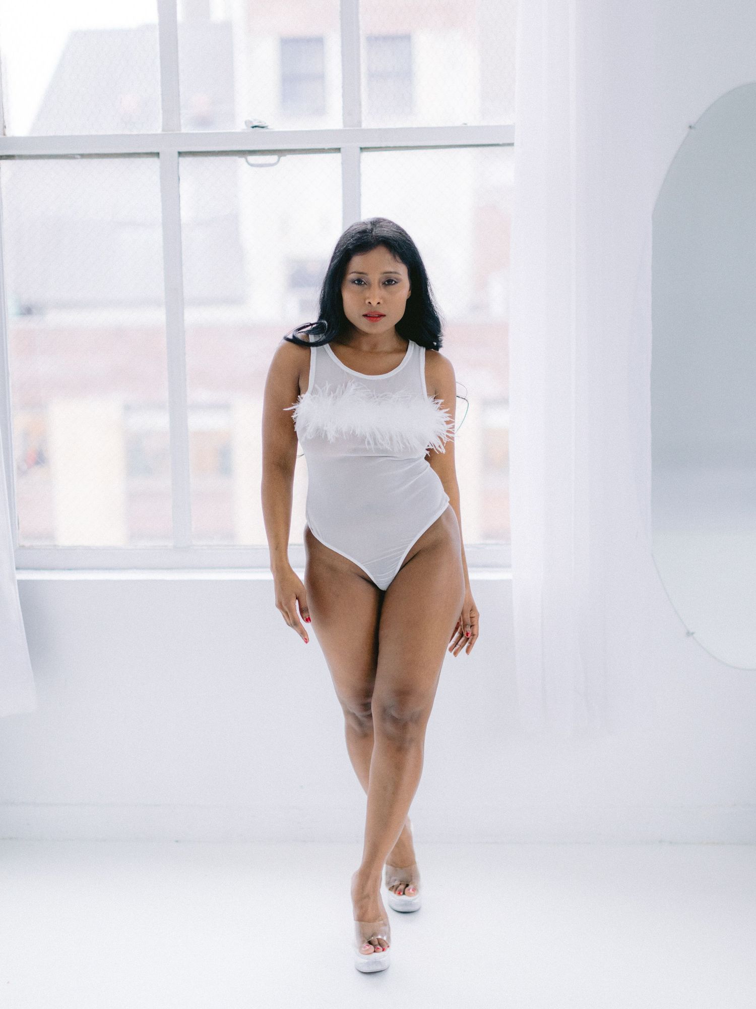 A woman in a white bodysuit performs dynamic dance movements across a bright minimalist studio space.