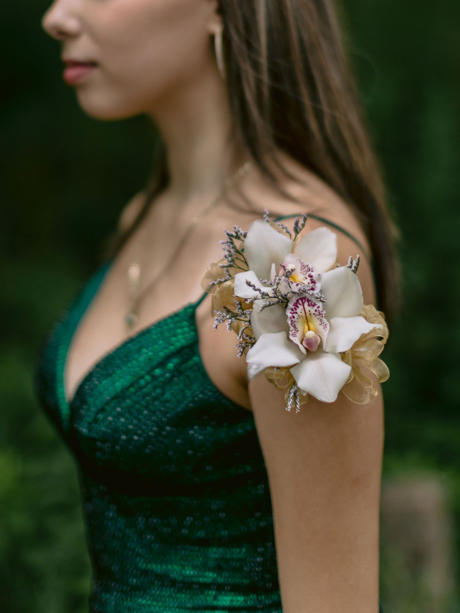 Close-up of white orchid corsage on shoulder of emerald green sequin formal dress.