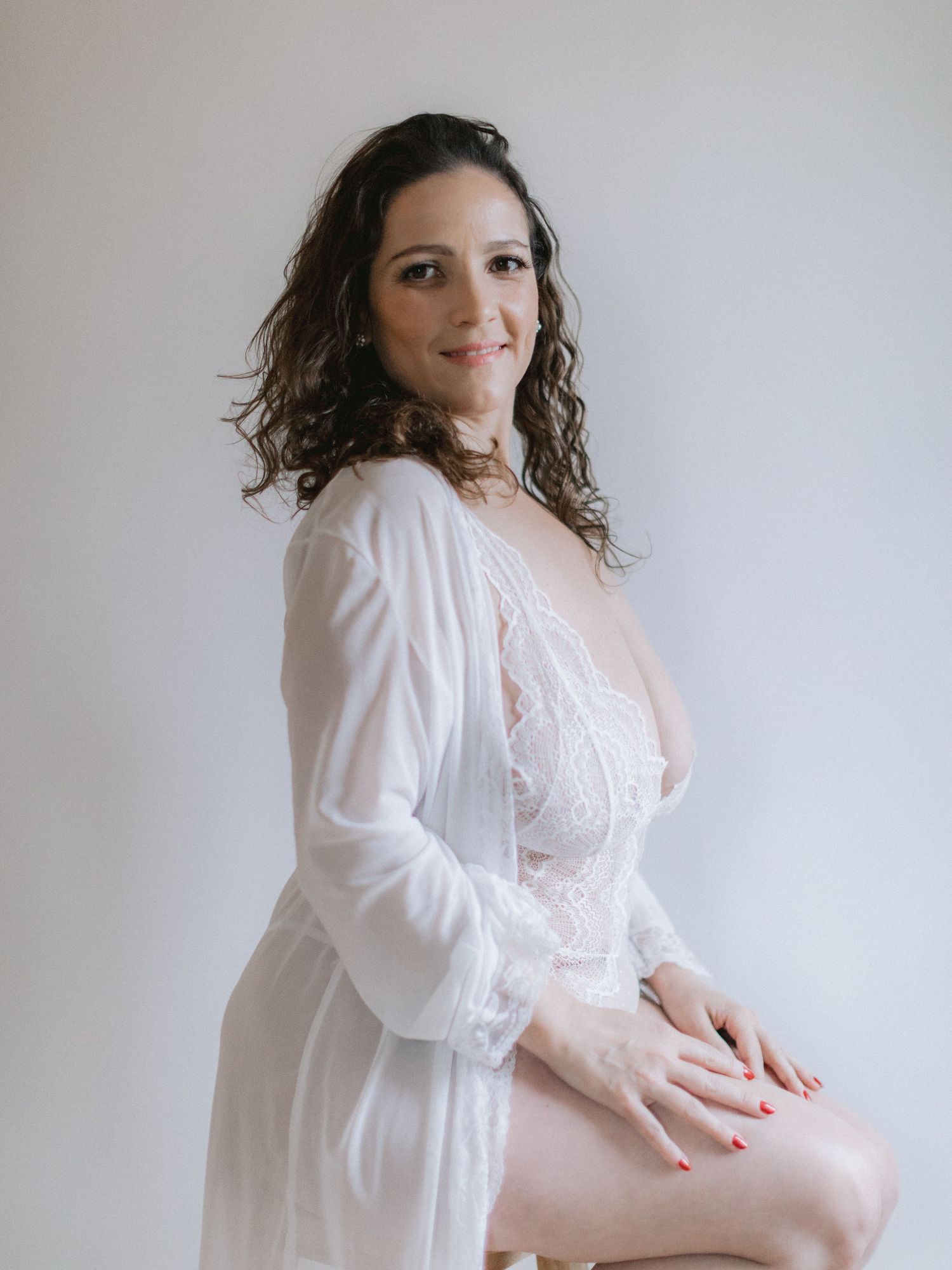 Intimate boudoir photo showing a woman in a flowing white dress against a light backdrop.