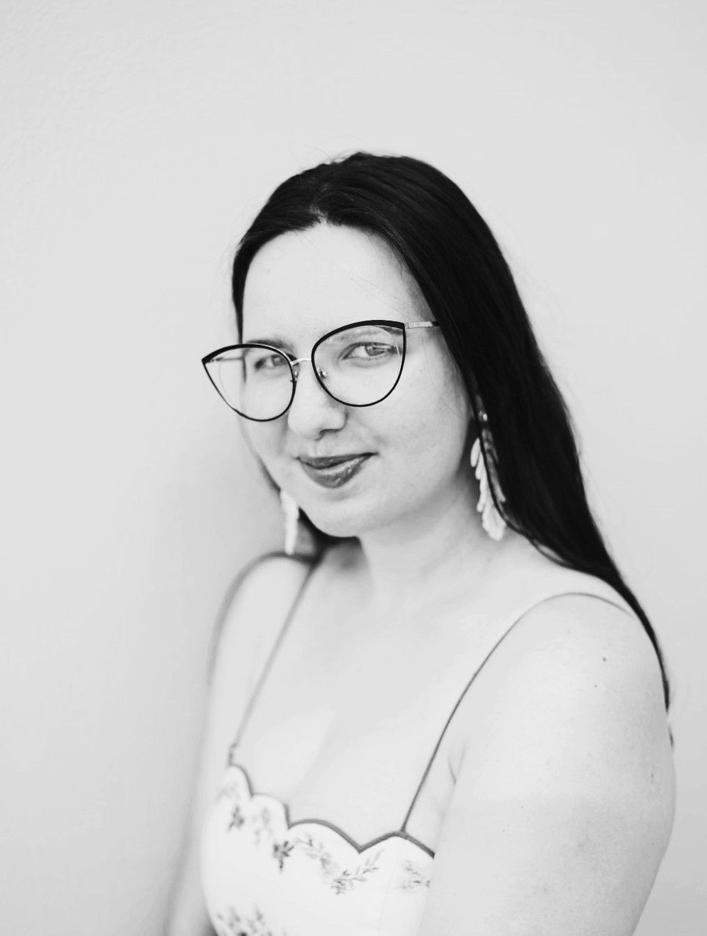Black and white portrait of a young woman with long dark hair wearing cat-eye glasses and a floral dress.