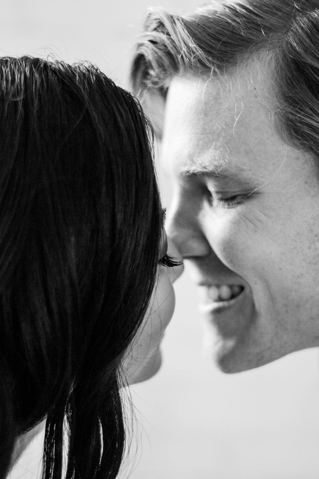 Black and white close-up portrait of a smiling couple touching foreheads romantically.