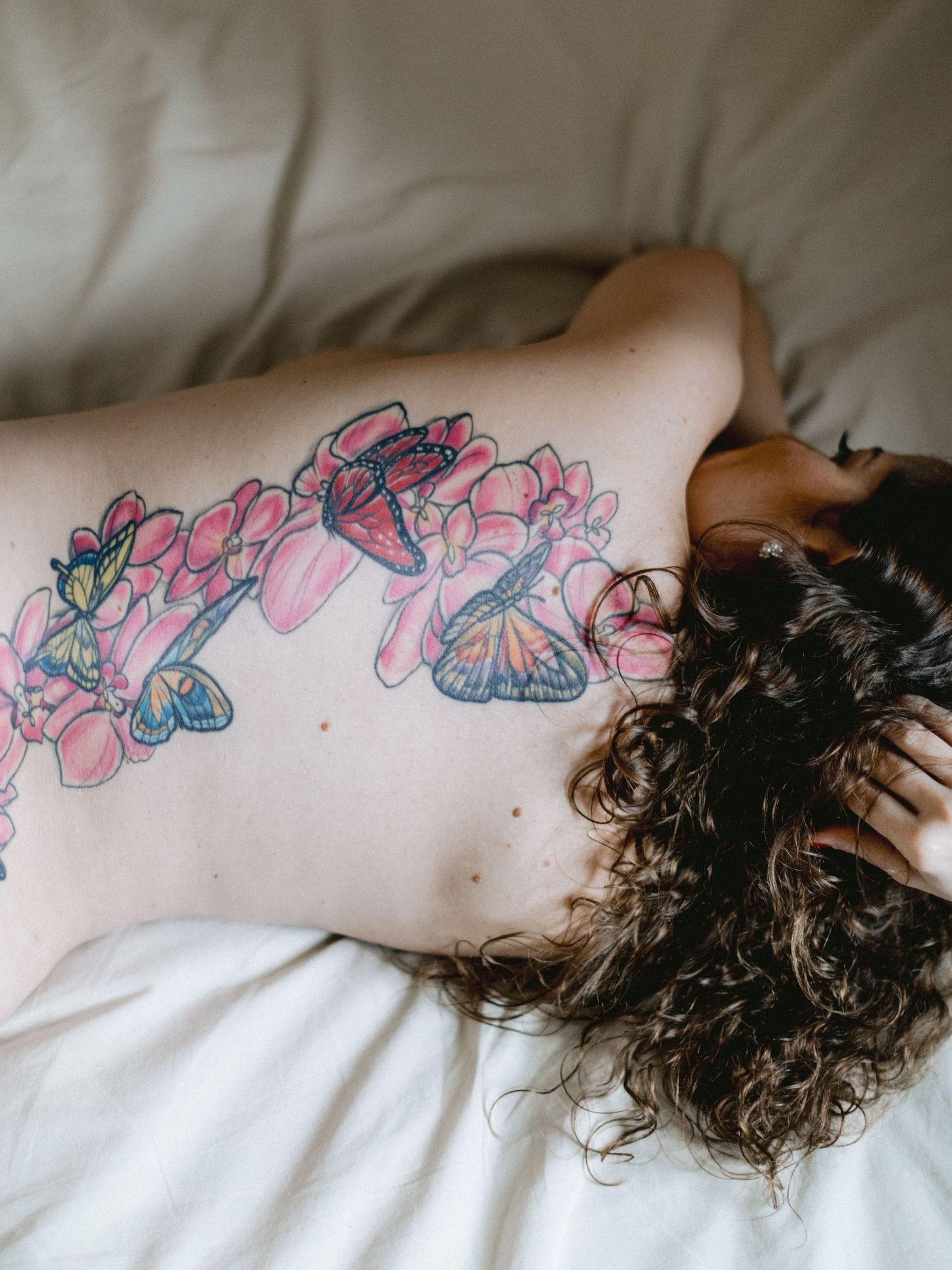 A delicate butterfly and floral tattoo design stretches across bare skin against white bedding.