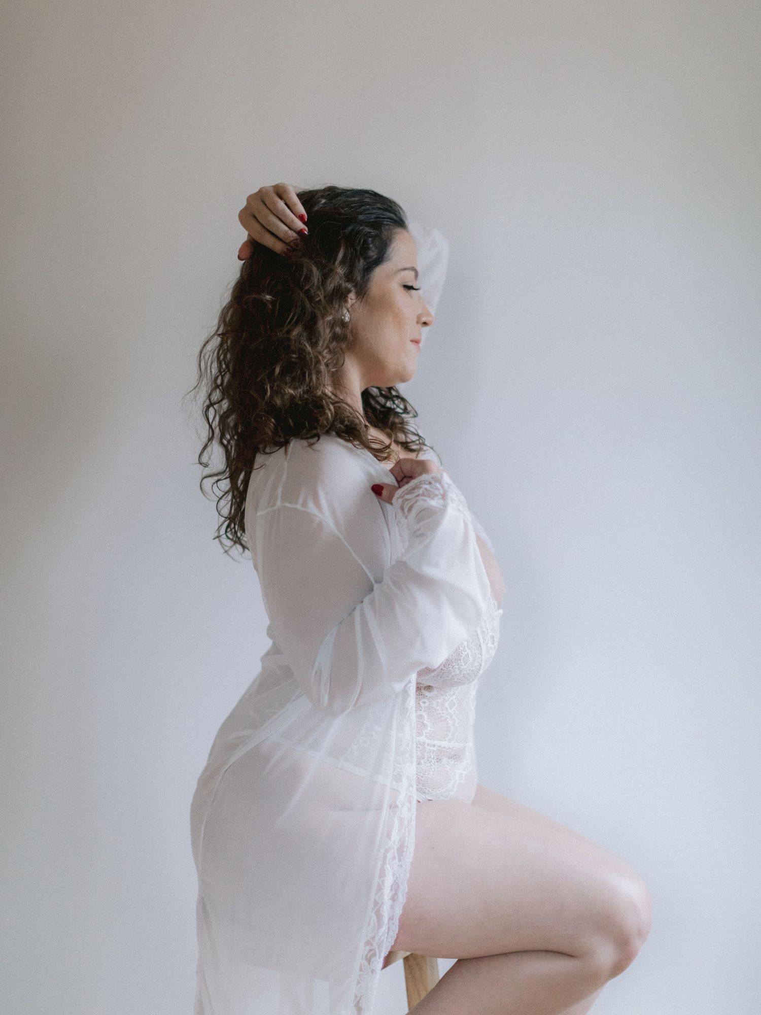 A boudoir photos showing a woman in a white button-down shirt against a light background.
