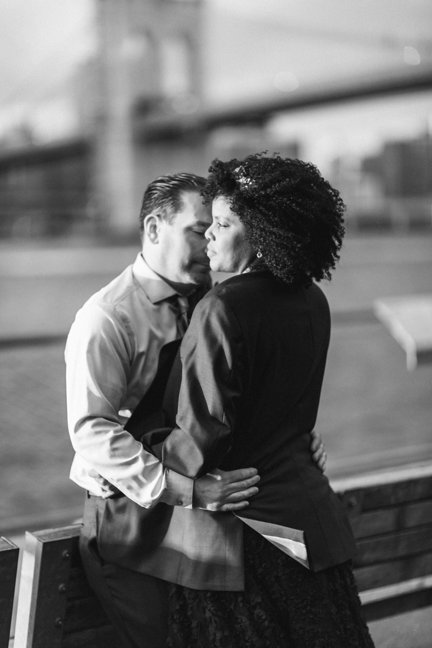 Black and white photo of couple embracing near Brooklyn Bridge waterfront in New York City.