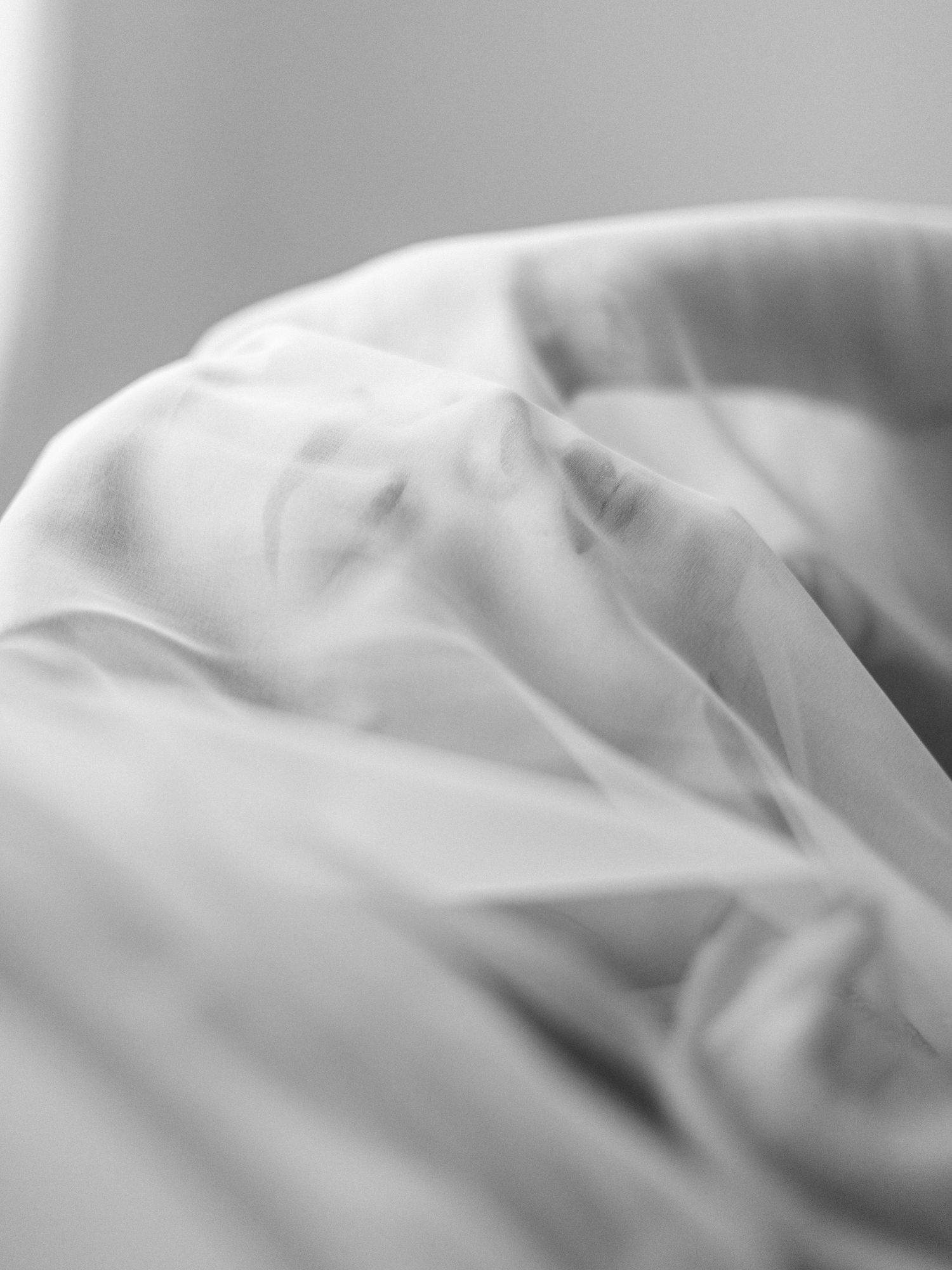 Black and white photo of a woman's face partially covered by sheer white fabric, creating a dreamy, ethereal effect.