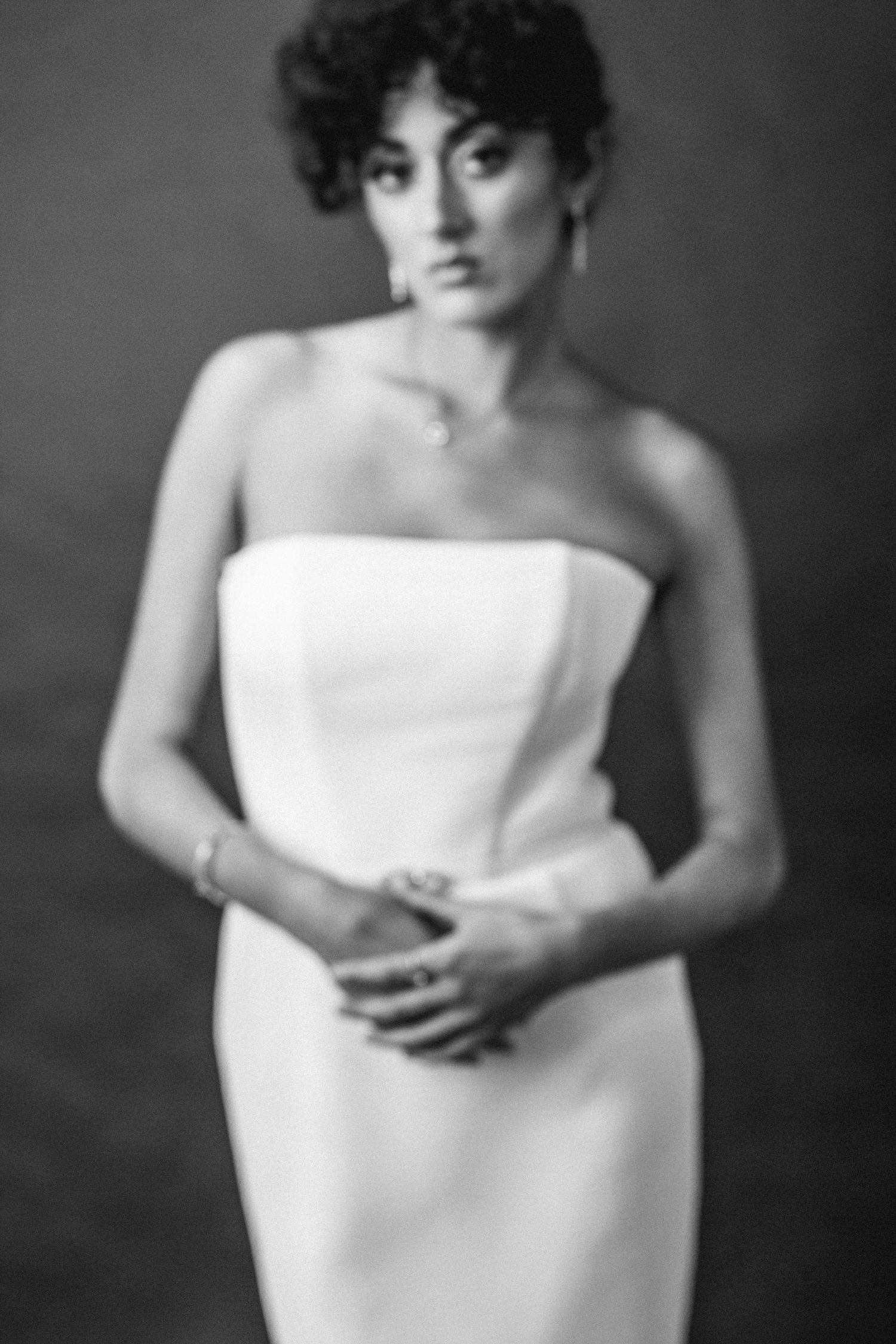 Black and white portrait of bride in strapless white sheath dress with curly updo hairstyle.