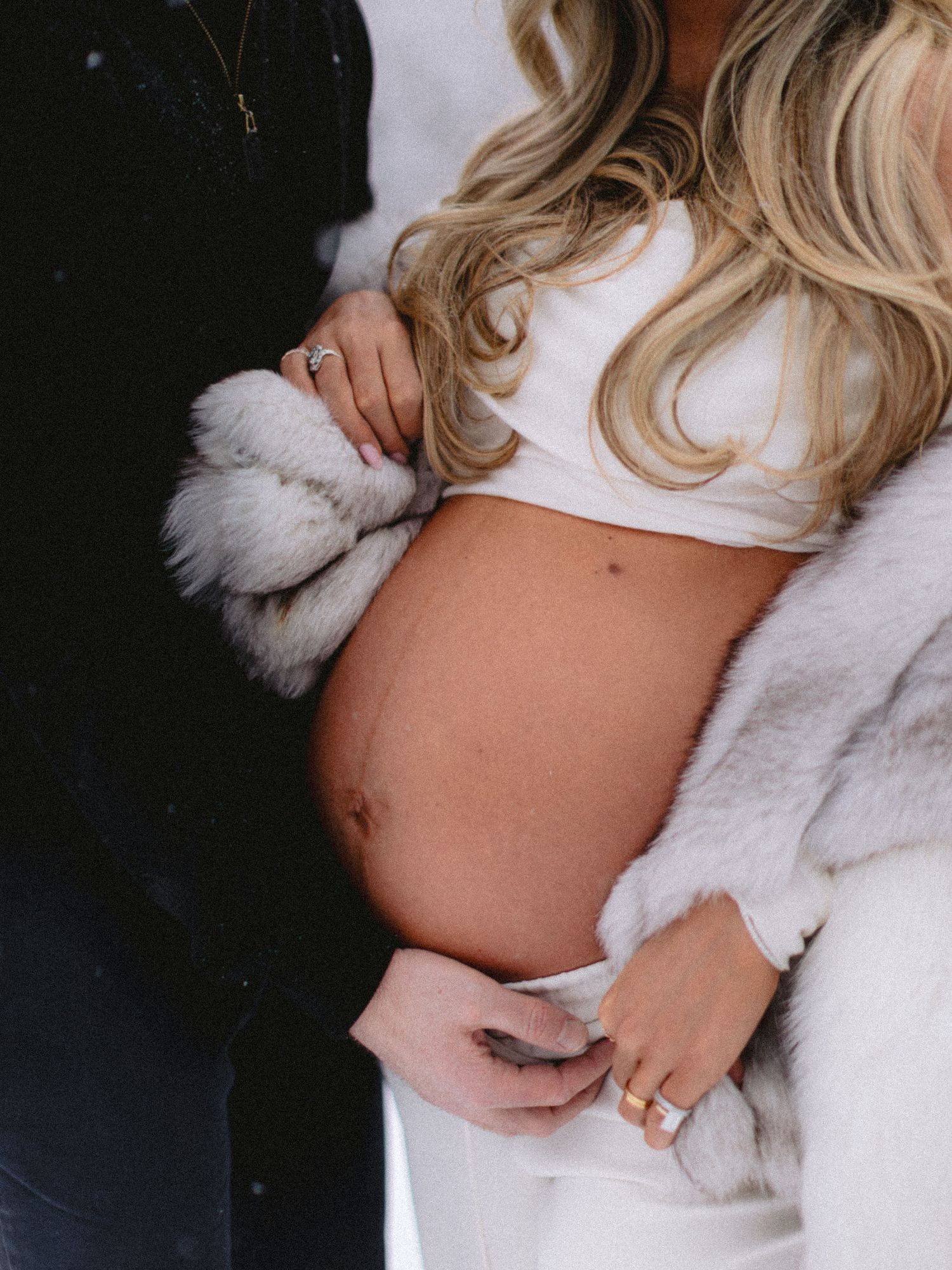 Close-up of pregnant woman's bare belly held by couple's hands outdoors in winter setting.