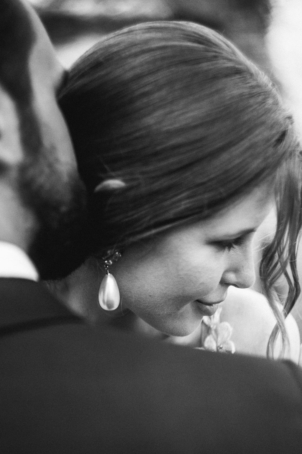 Black and white close-up of bride with pearl drop earring smiling softly during wedding ceremony.