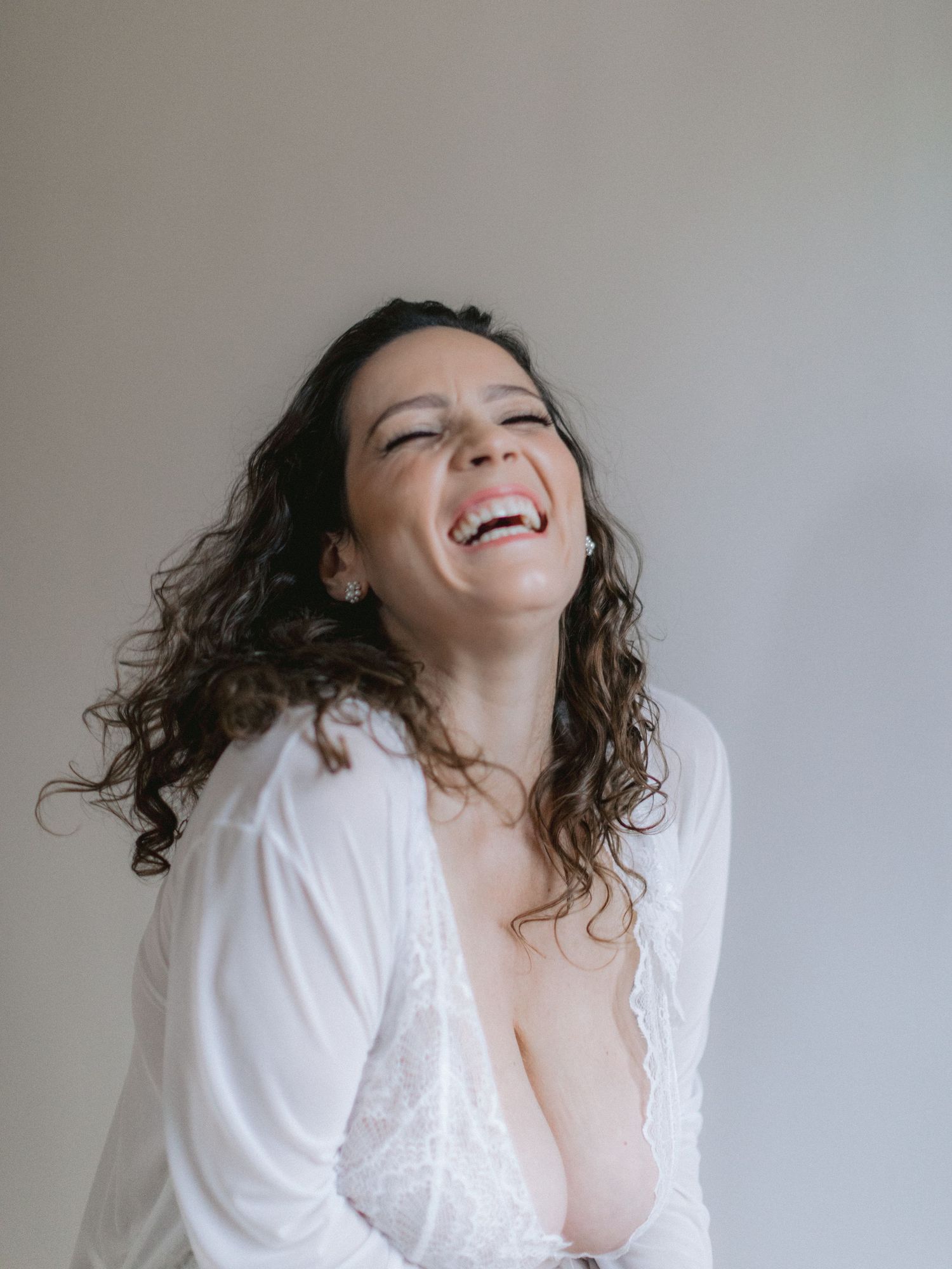 A photo of a woman with curly hair in a white lace top expressing joyful laughter.