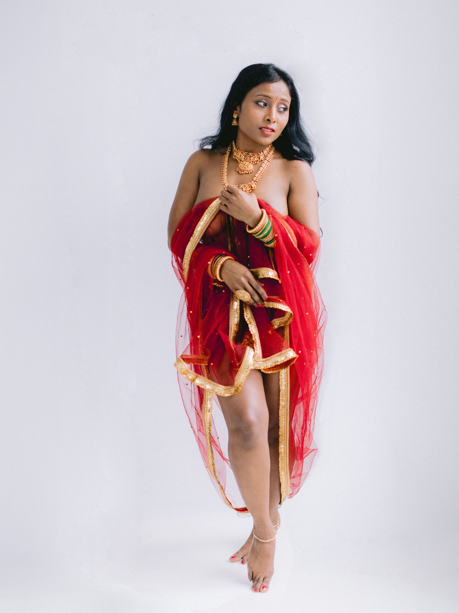 Artistic portrait showing a woman in red flowing fabric posing gracefully against a white backdrop.