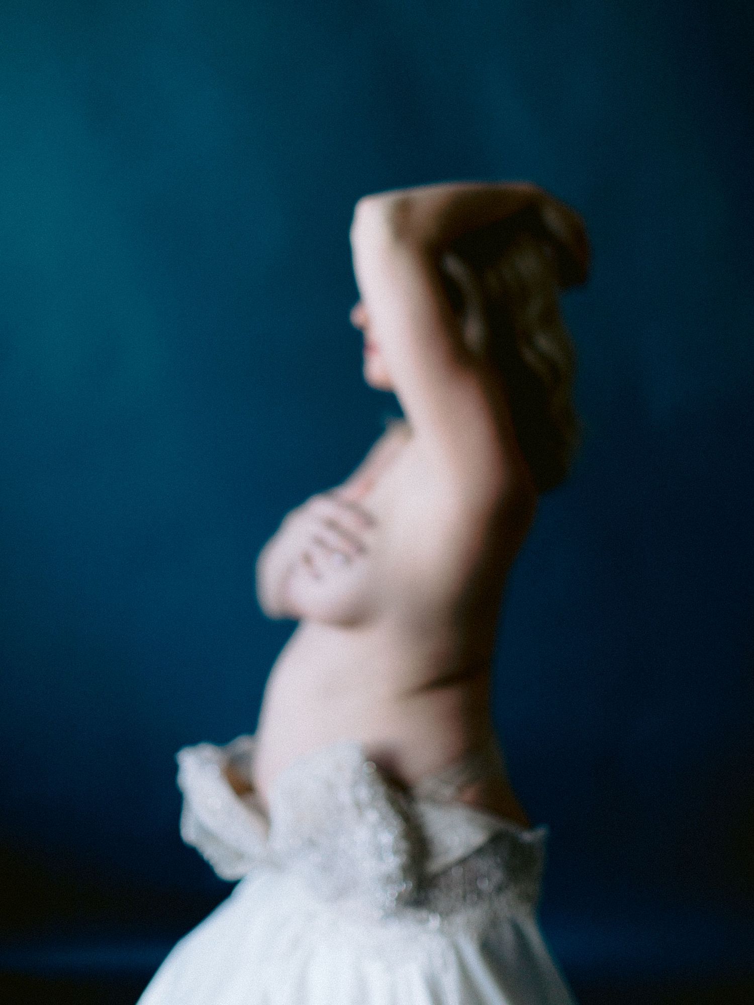Blurred artistic profile of a philadelphia maternity woman in a white wedding dress against a deep blue background.