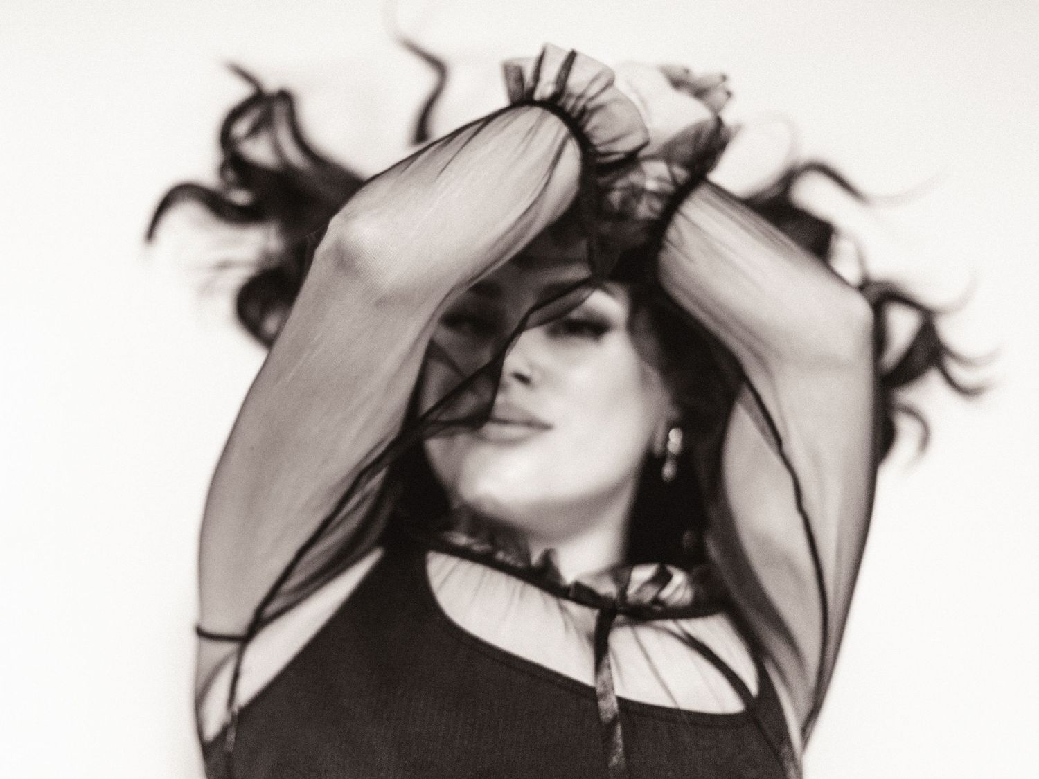 Artistic black and white portrait of woman with flowing hair and sheer black top.