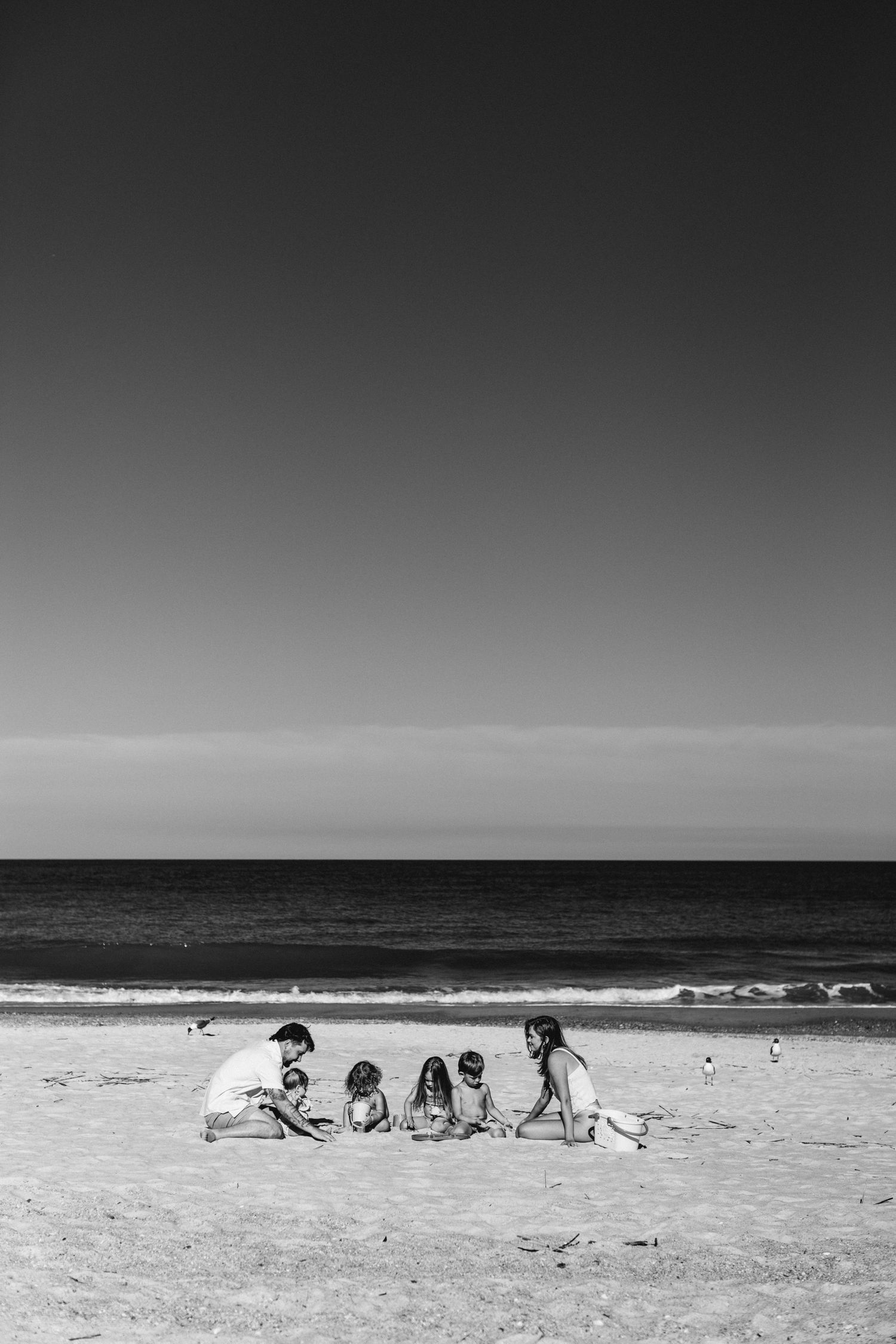 Black and white photo of a family playing together on a sandy beach with calm ocean waves in the background.